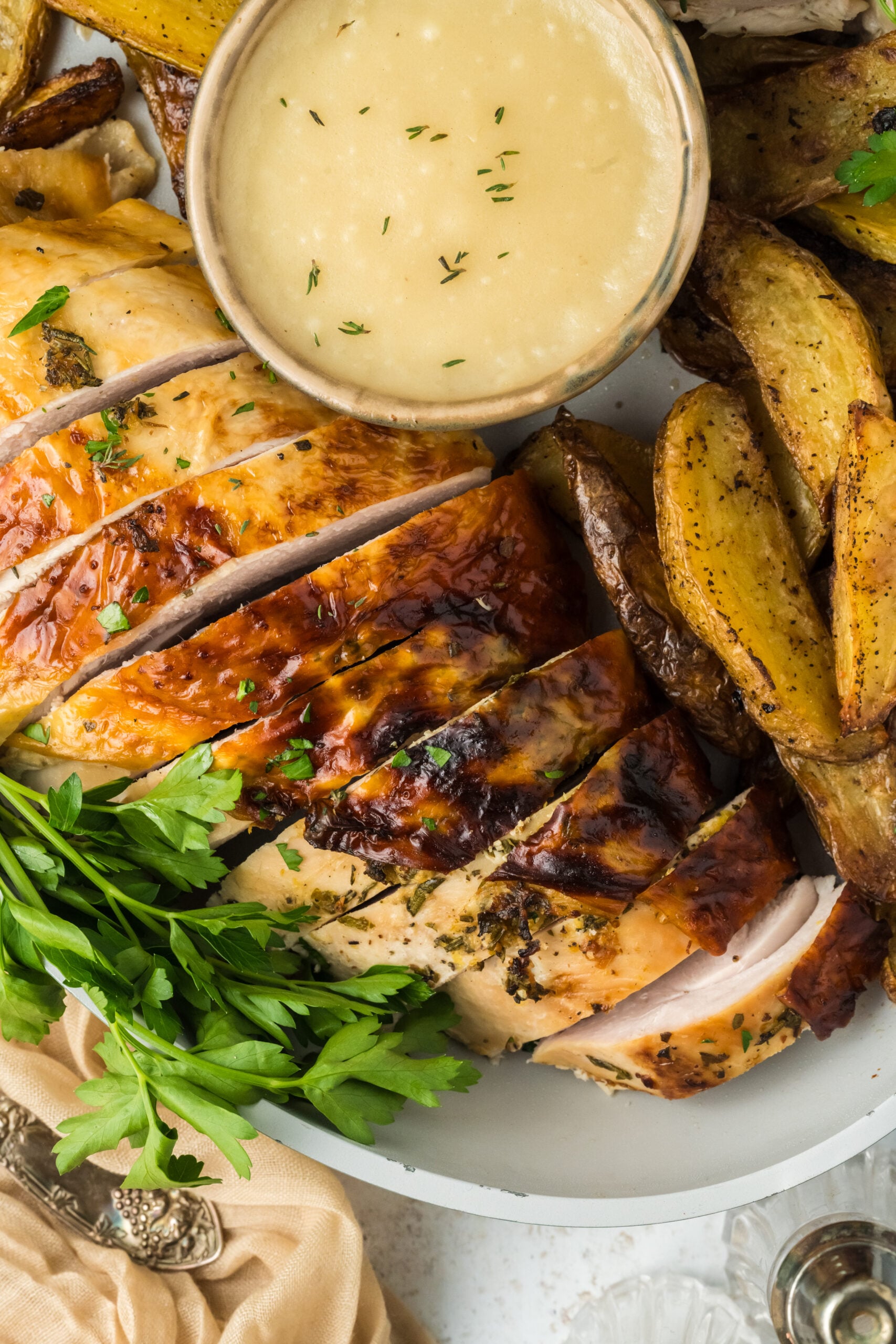 up close view of a big white platter with sliced roasted turkey on it with roasted potatoes