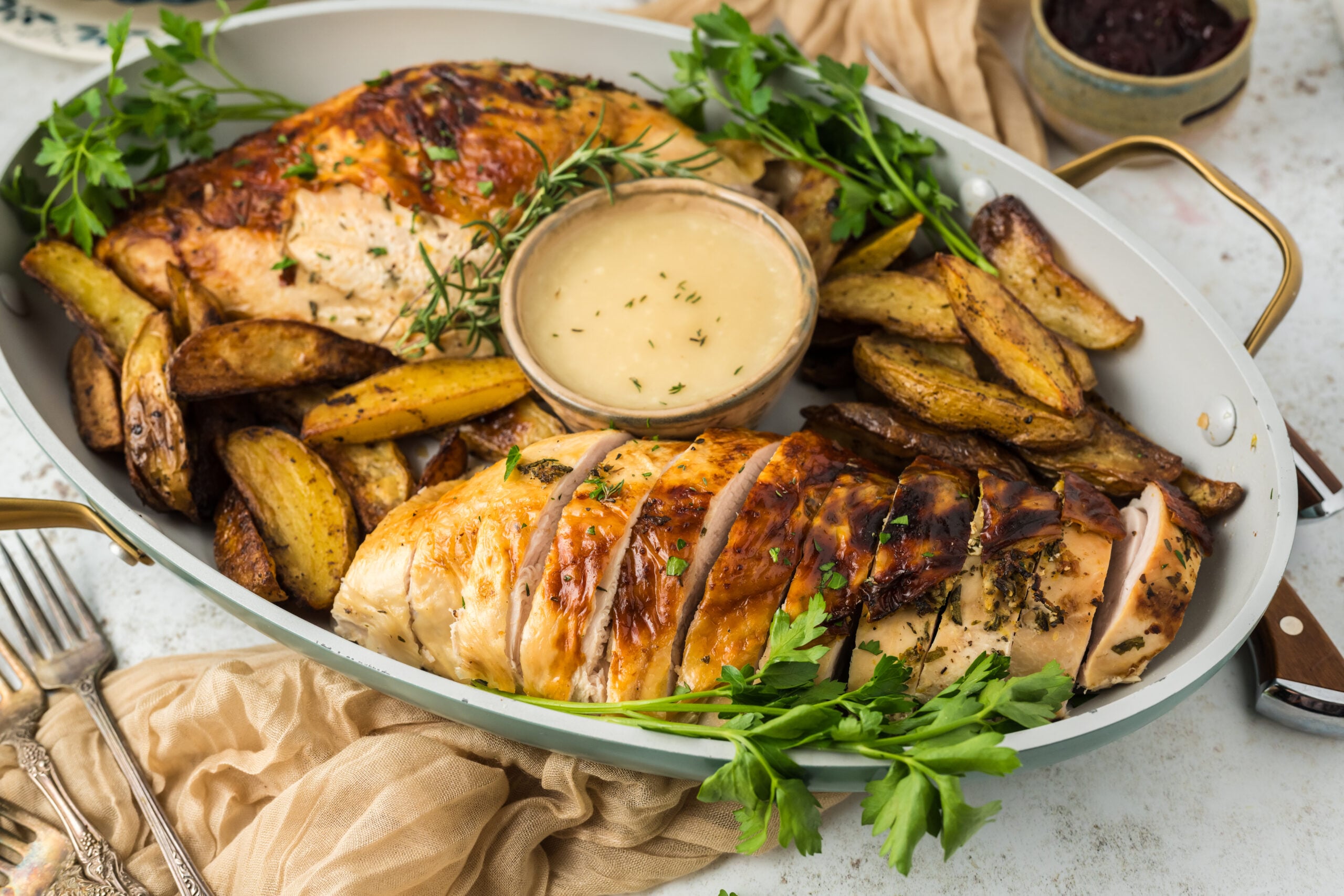 large platter on white table with sliced roasted turkey on it, with a bowl of sauce and roasted potatoes