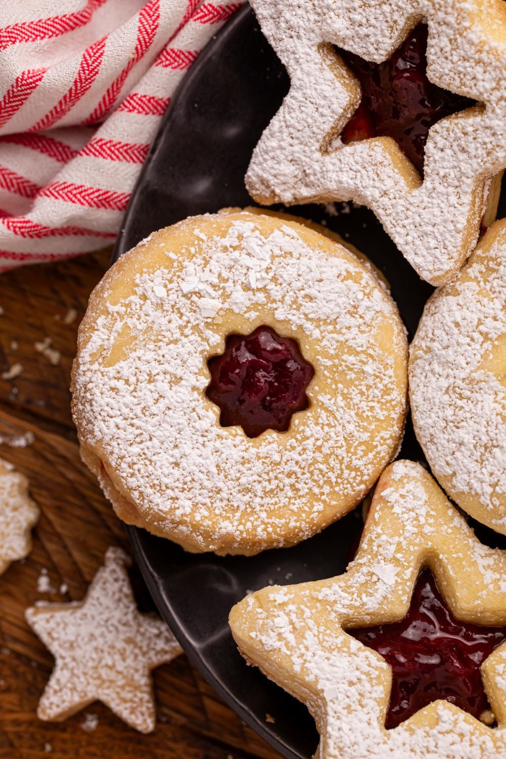 close up of Linzer cookies on a black plate dusted with powdered sugar