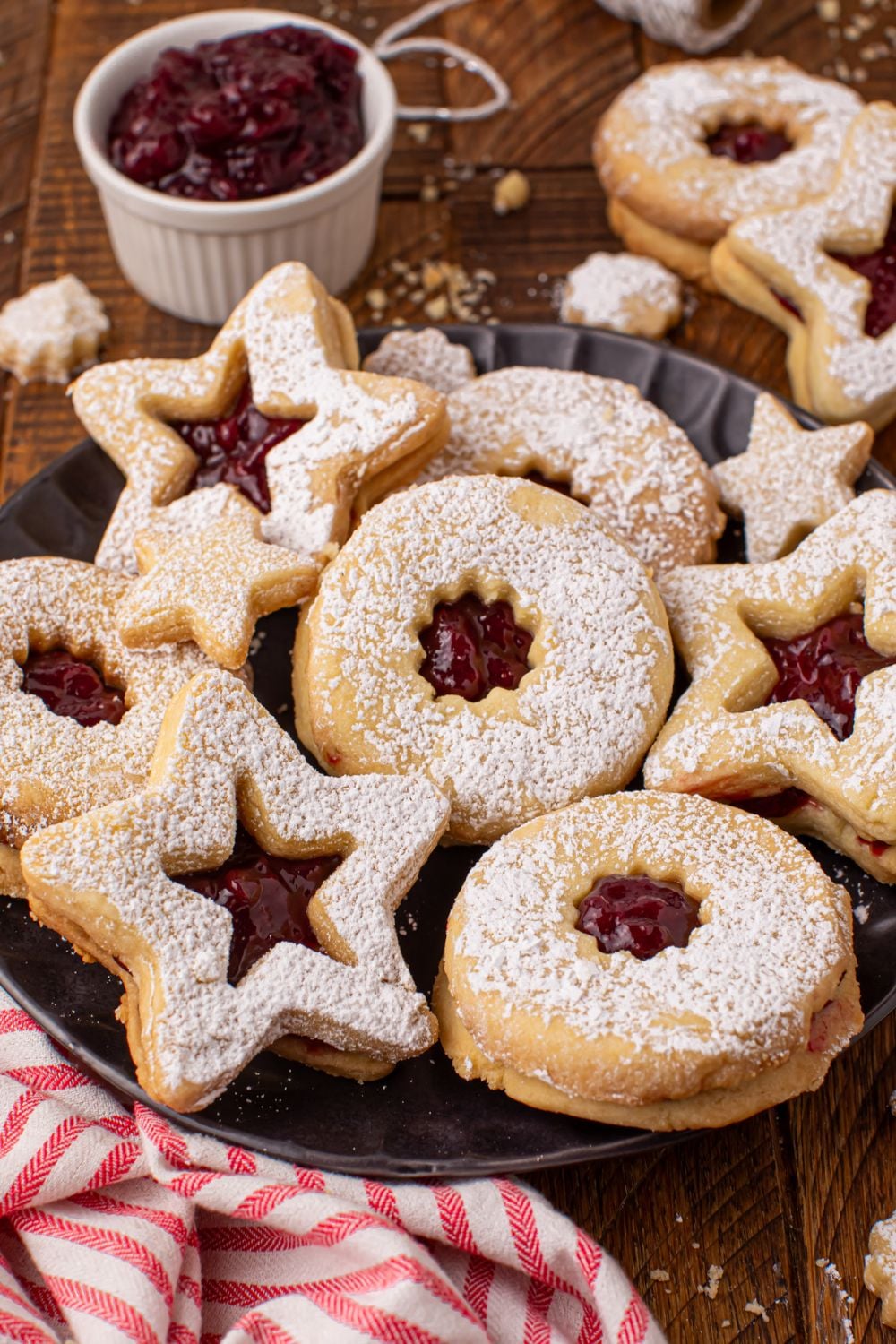 Linzer cookies on a plate with a red striped towel and a white bowl of jam to side