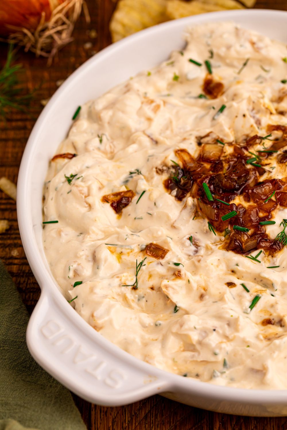 side view of a bowl full of Caramelized Onion Chip Dip with chips behind it on the table 