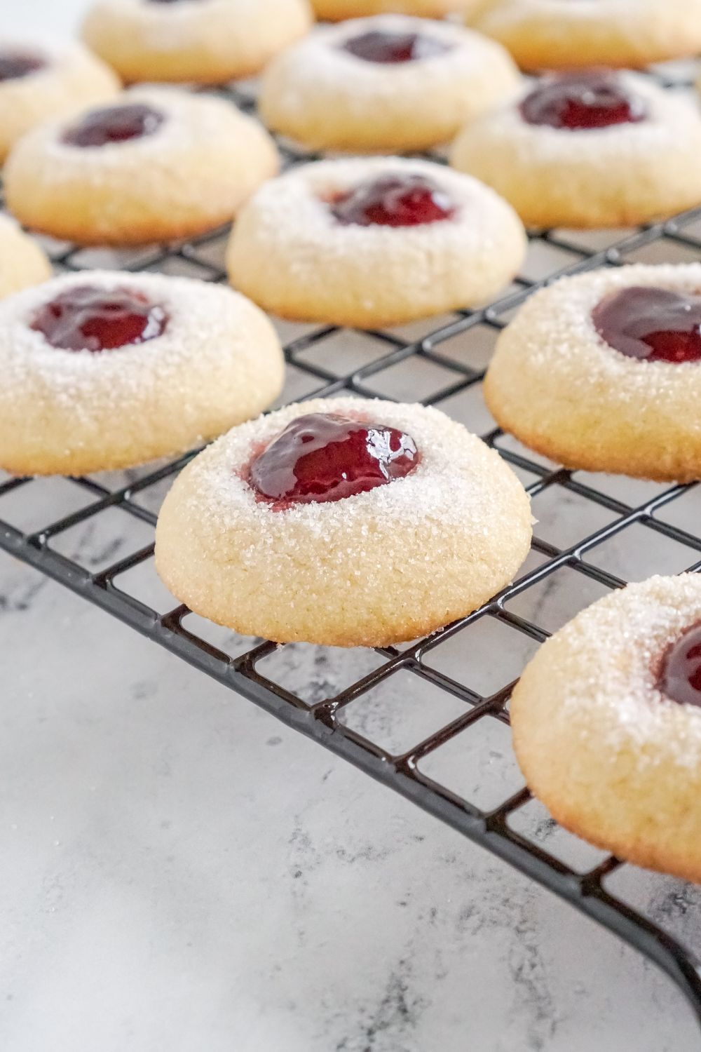 Raspberry Thumbprint Cookies on a cooling rack on a marble counter showing a side of the cookies