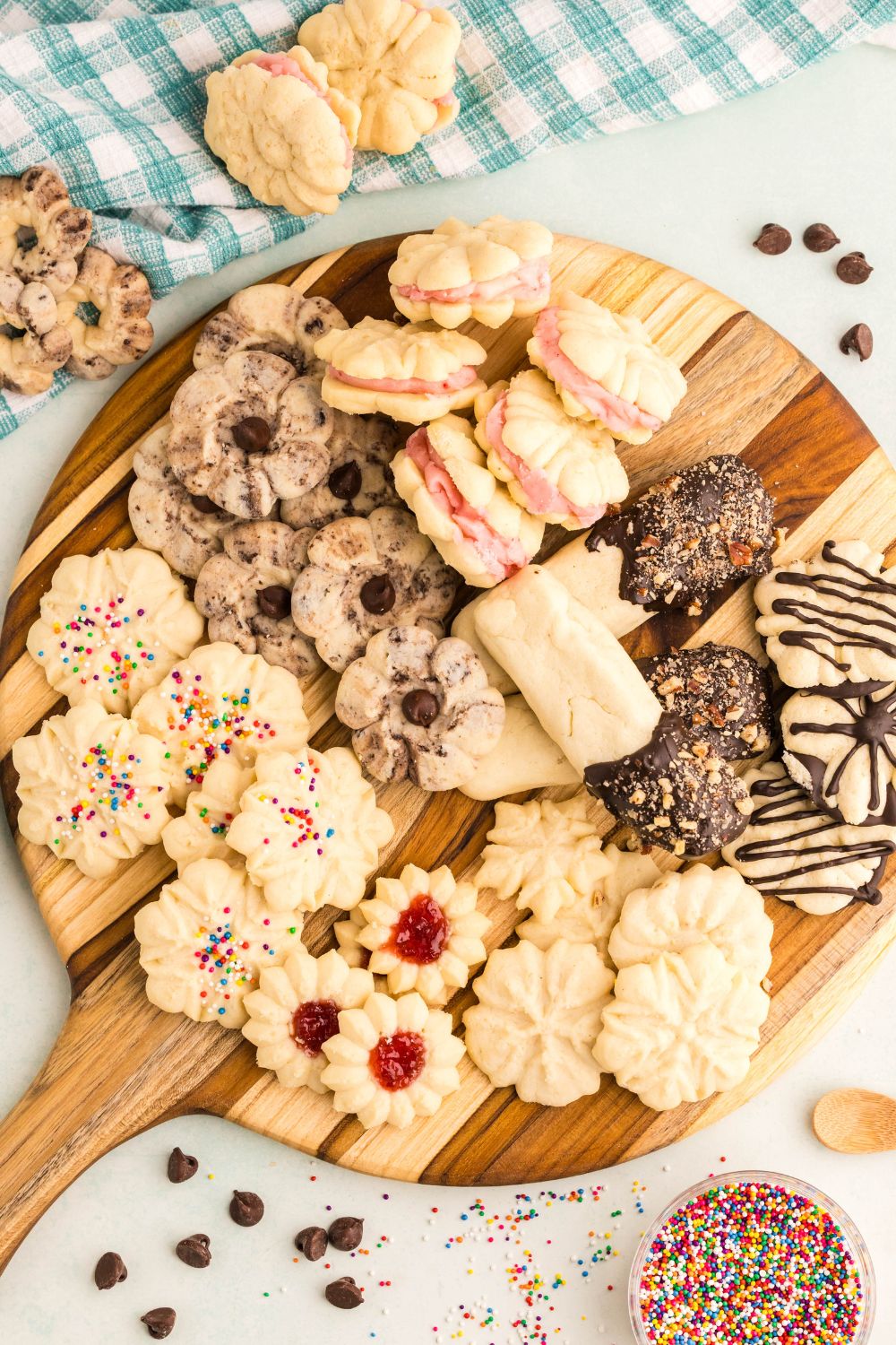 Spritz Christmas Cookies on a wooden tray with a checkered towel to side