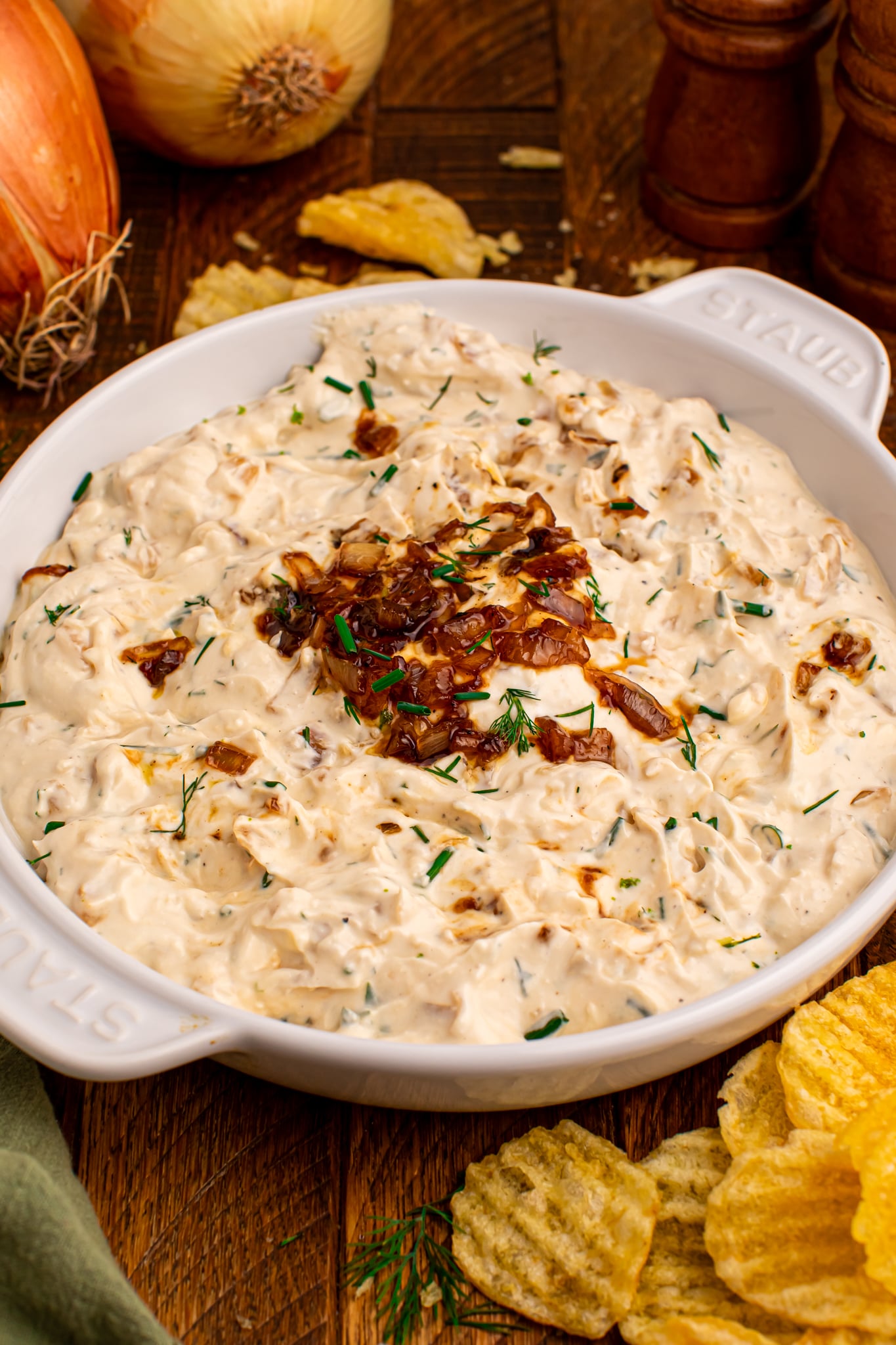 Caramelized Onion Chip Dip in a white staub bowl on dark wooden table with chips to the side 