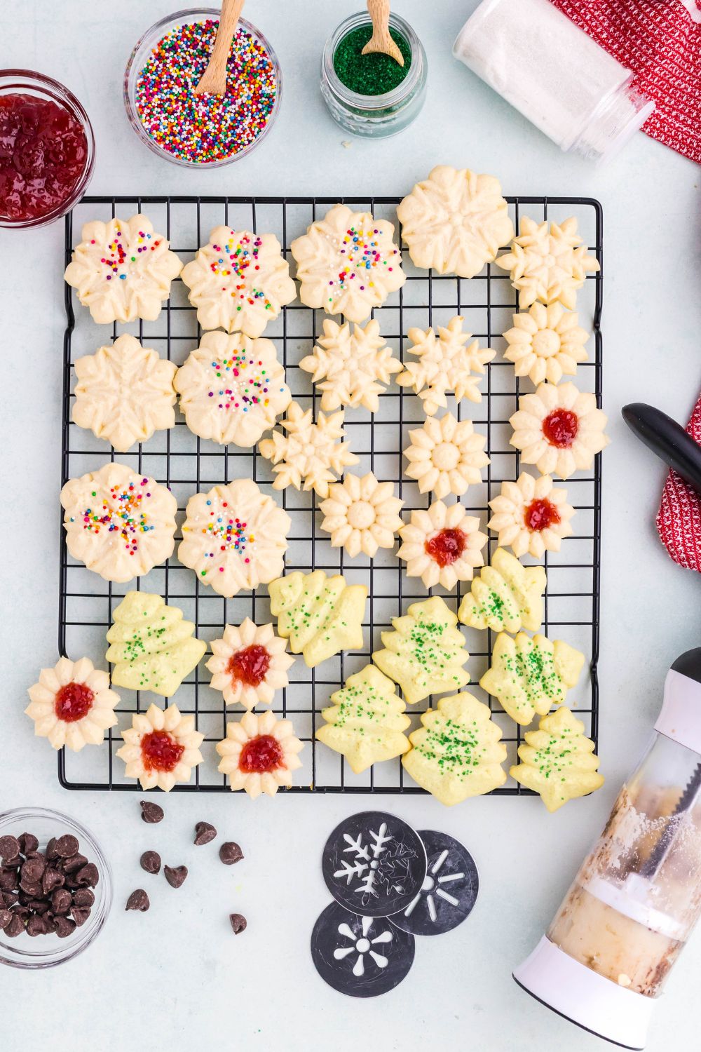 cooling rack full of decorated Spritz Christmas Cookies and the fillings and sprinkles around the table