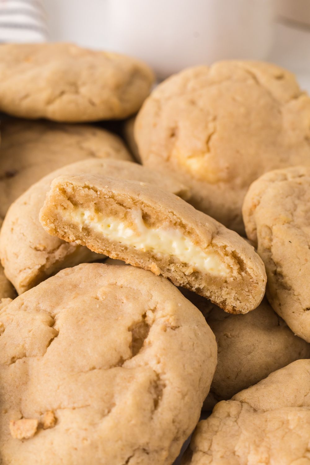 New York cheesecake cookies stacked on table with one cut in half to show the creamy filling in the cookies 