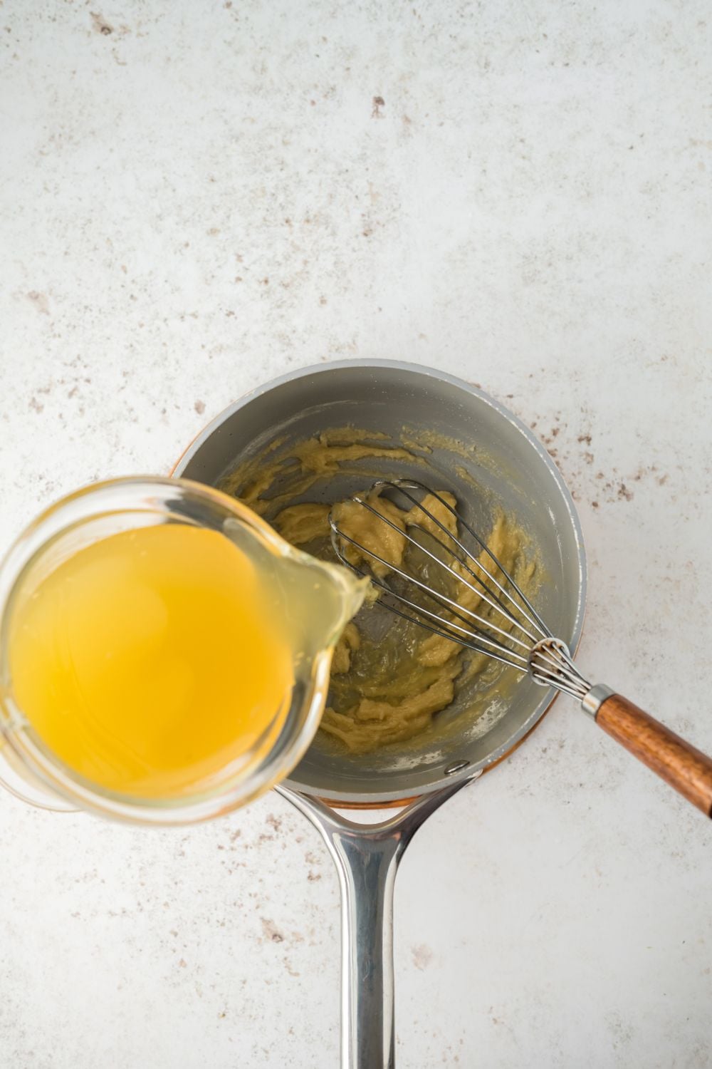 roux in saucepan with stock pouring into the pan to make a gravy
