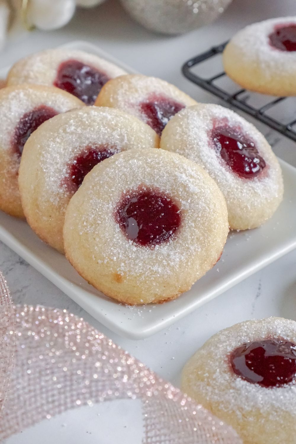 white tray on counter with two rows of Raspberry Thumbprint Cookies and ribbon in front of bowl