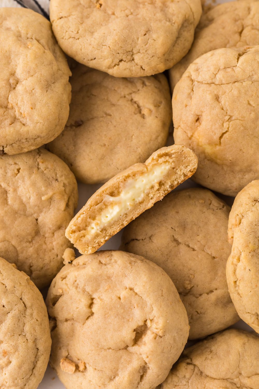 New York cheesecake cookies spread out on table with one cut in half and tilted on side to show the cheesecake filling 