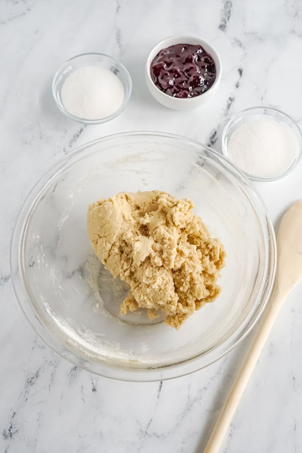 cookie dough in glass bowl on marble counter with other bowls of ingredients to side
