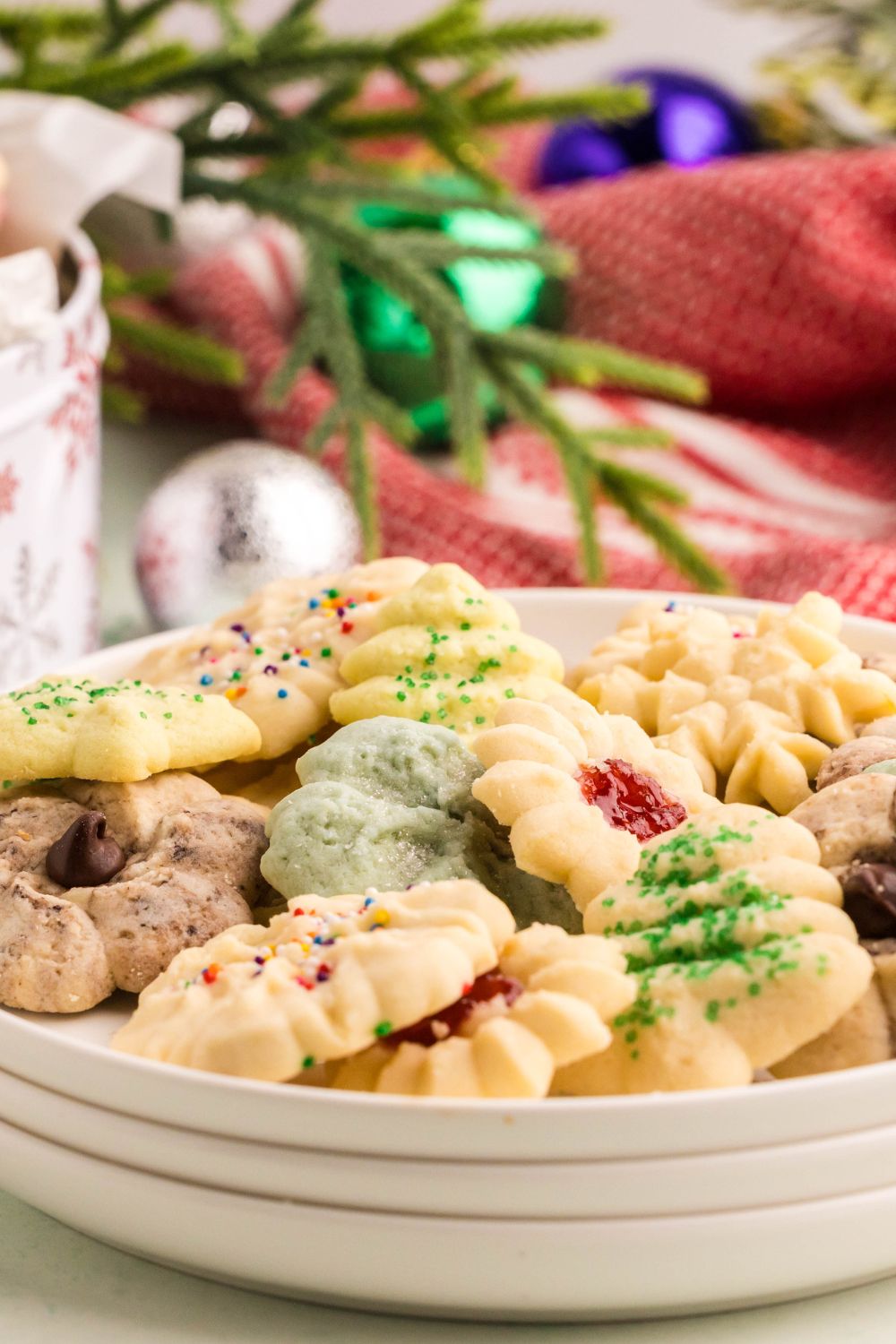a stack of white plates with the top plate full of Spritz Christmas Cookies with a Christmas themed table