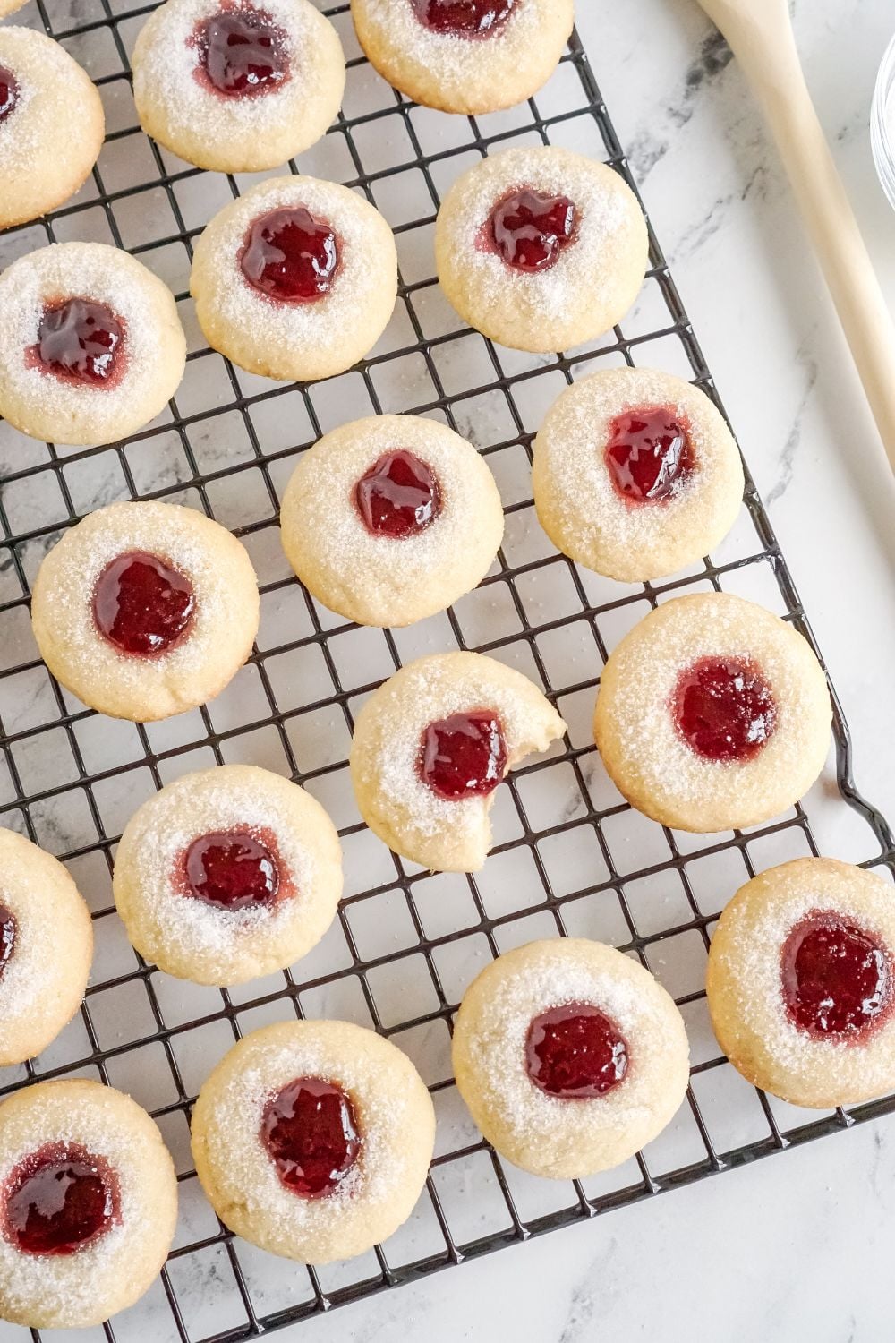 cooling rack with Raspberry Thumbprint Cookies with bites taken out of one of those cookies
