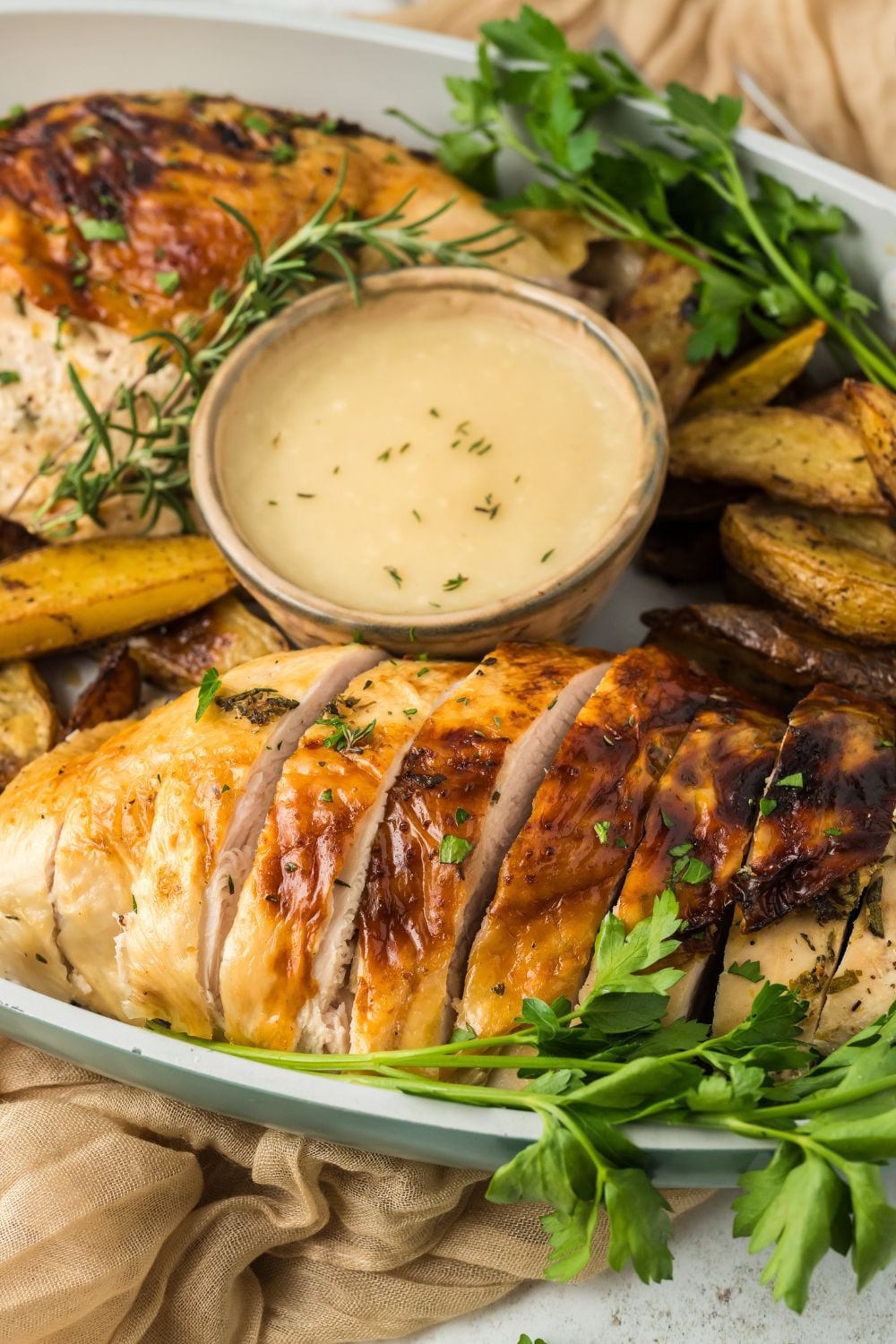 a large platter on table with sliced turkey breast that has been roasted and a bowl of sauce for dipping