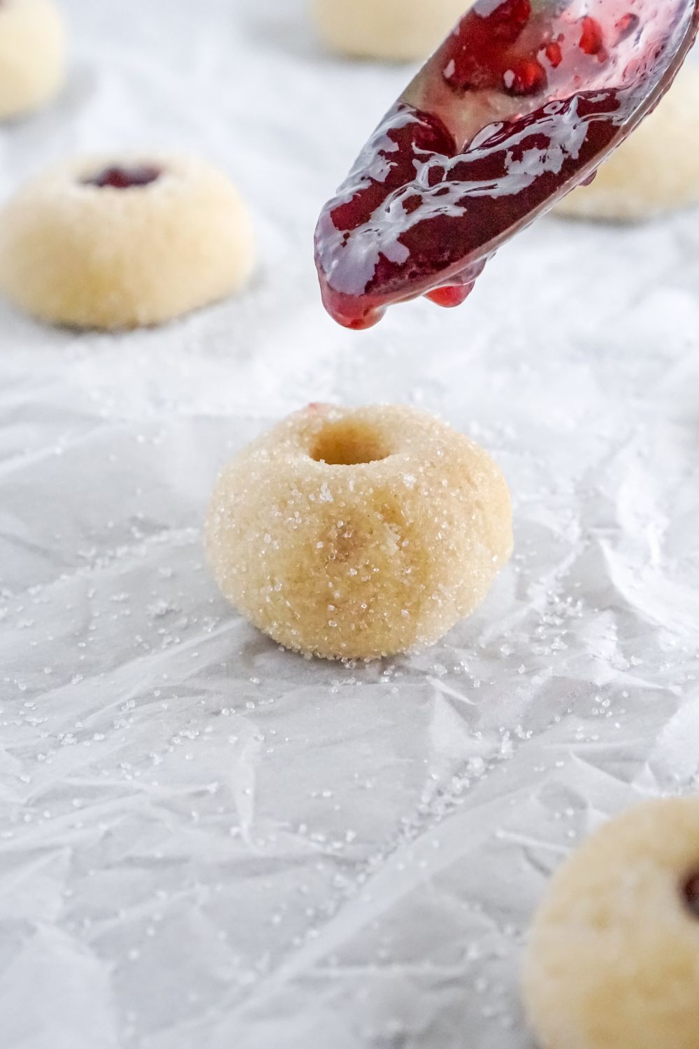 raw cookie dough with a spoon of jam pouring in the center of each Raspberry Thumbprint Cookie