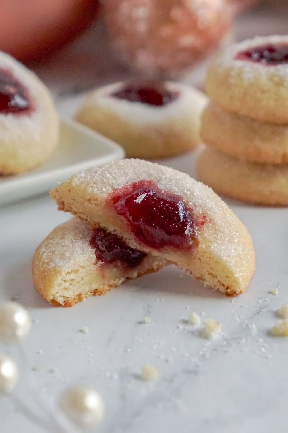 Raspberry Thumbprint Cookie cut in half and placed on table with a stack of cookies behind it on table