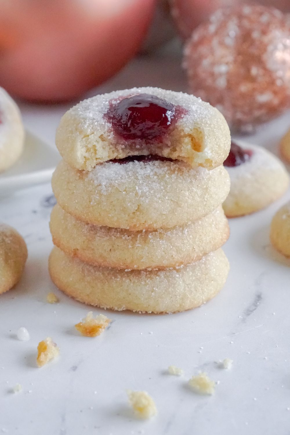 Raspberry Thumbprint Cookies in a stack on table with a bite taken out of the top cookie in the stack