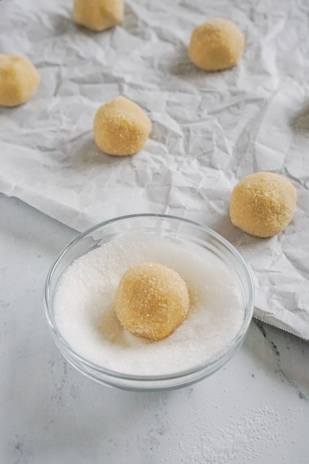 cookie dough being rolled in a small bowl of sugar by baking sheet