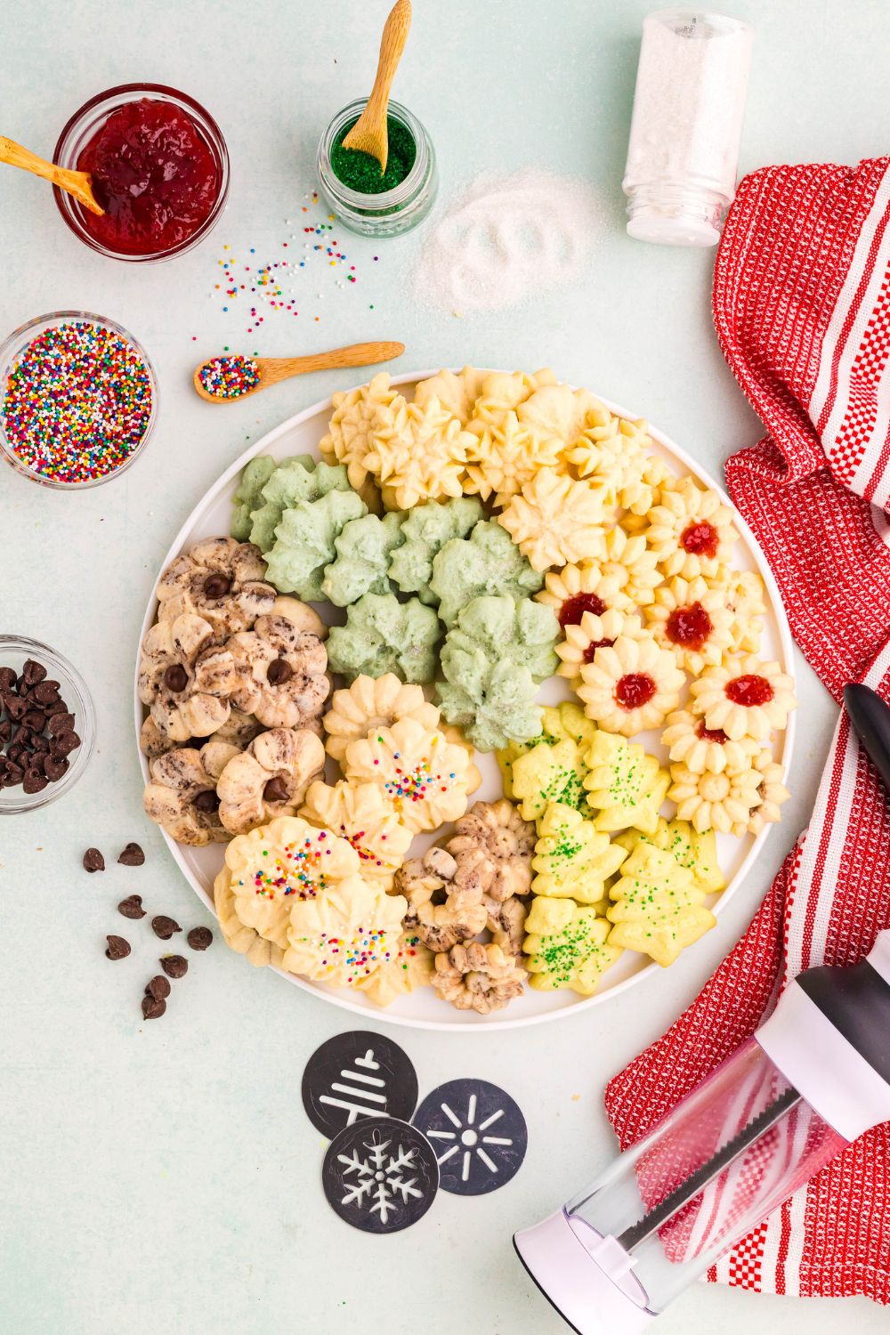 a large platter with a mix of Spritz Christmas Cookies with a jar of jam, sprinkles, and more around the platter