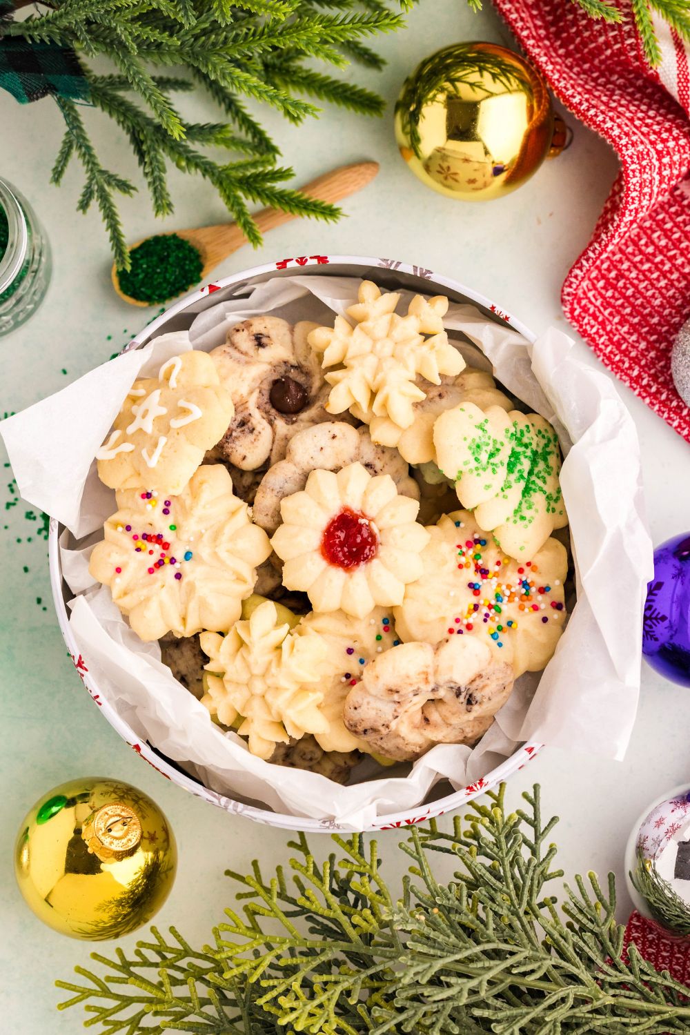 metal tin full of Spritz Christmas Cookies with a mix of designs with faux tree and ornaments around the table