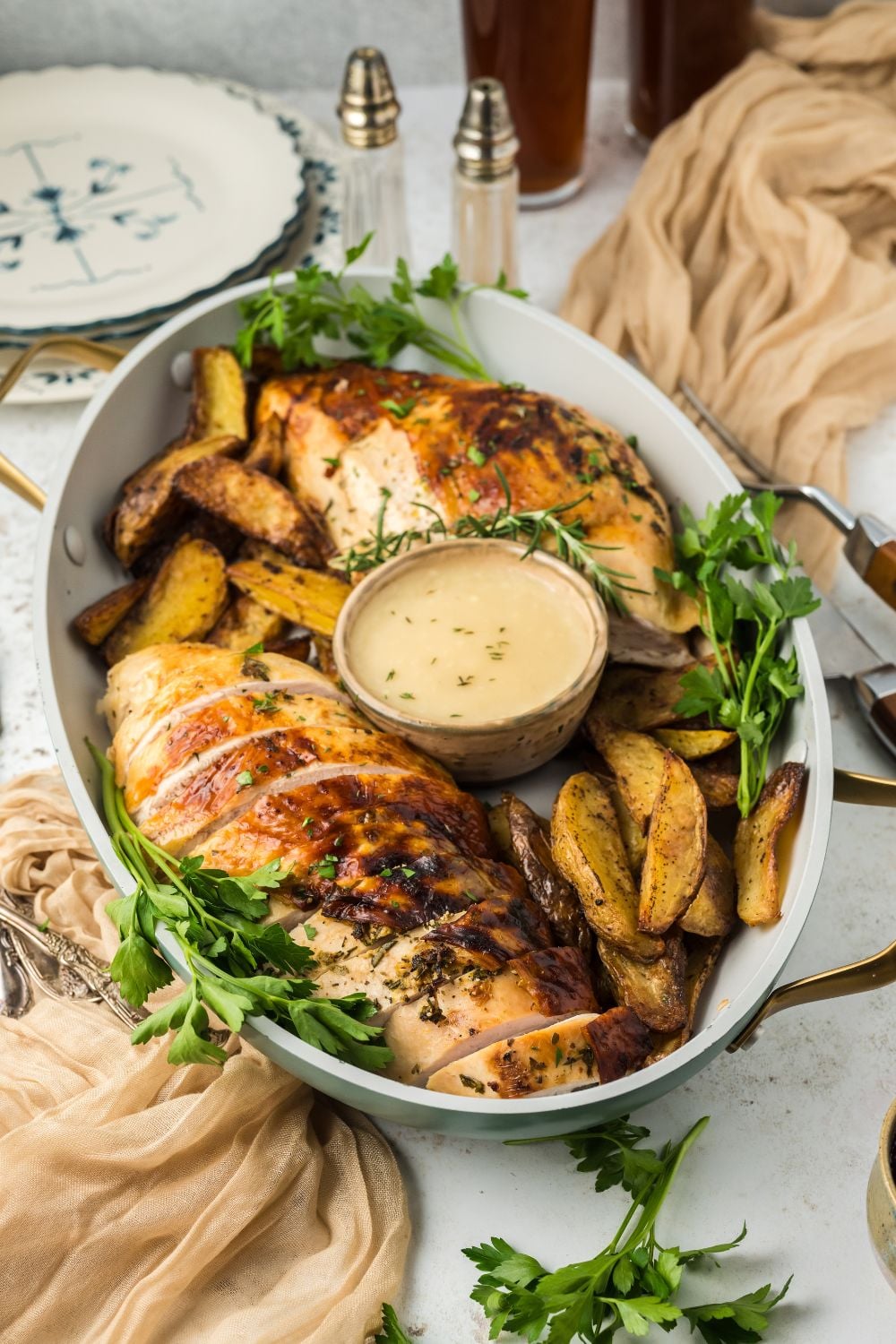 Roasted Turkey Breast in a platter on white table full of potatoes, greens, and a small bowl of gravy in center of the platter