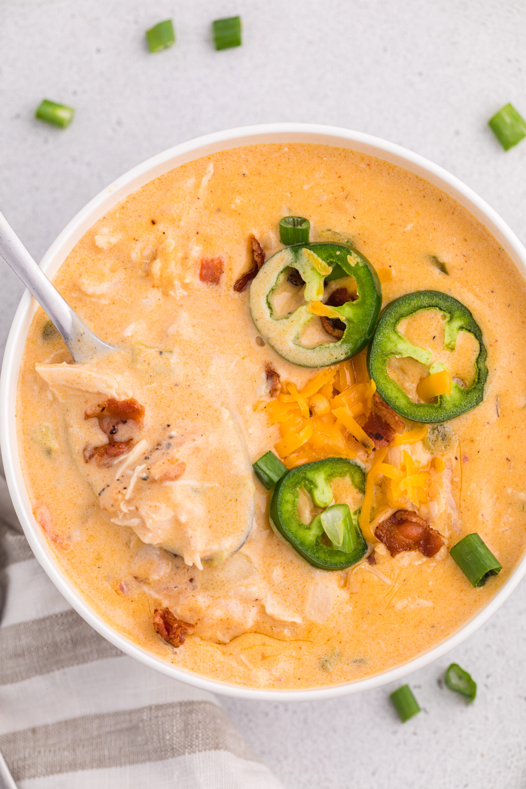 overhead shot of a white bowl filled with jalapeño popper crack chicken soup with a spoon scooping up some of the soup