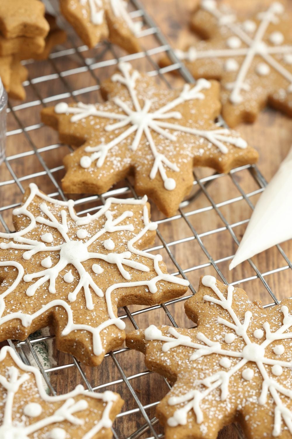 snowflake gingerbread cookies on a cooling rack being decorated with royal icing 