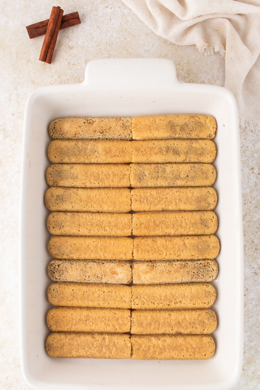 a single layer of dipped ladyfinger cookies in a white casserole pan 