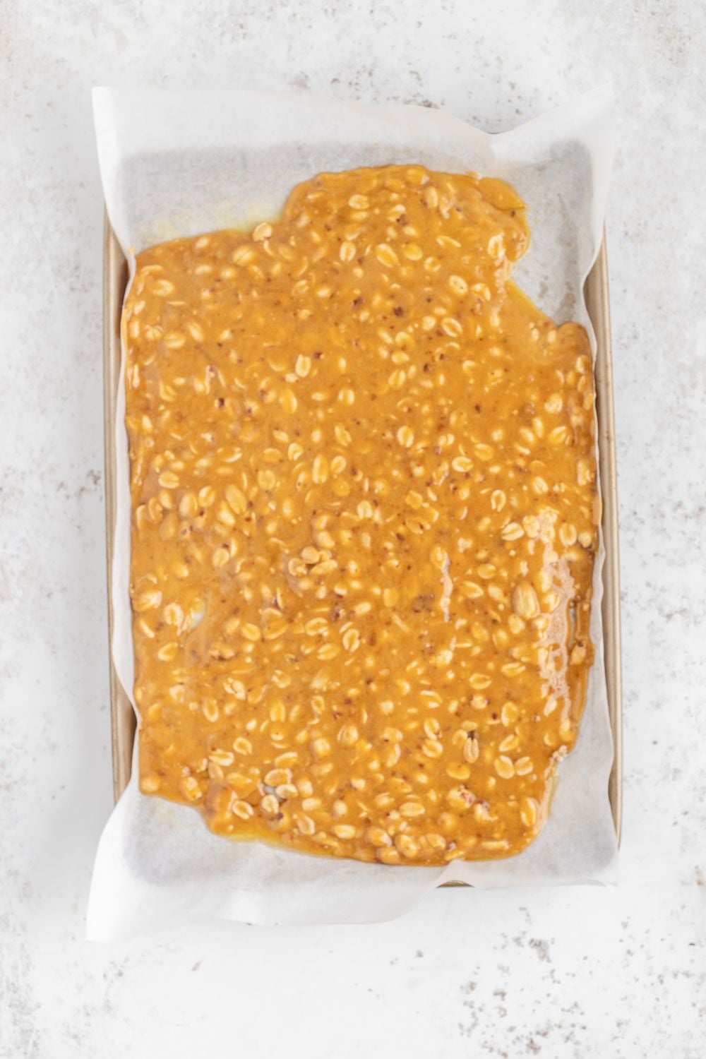 sheet pan with parchement paper with a spread out of Homemade Peanut Brittle
