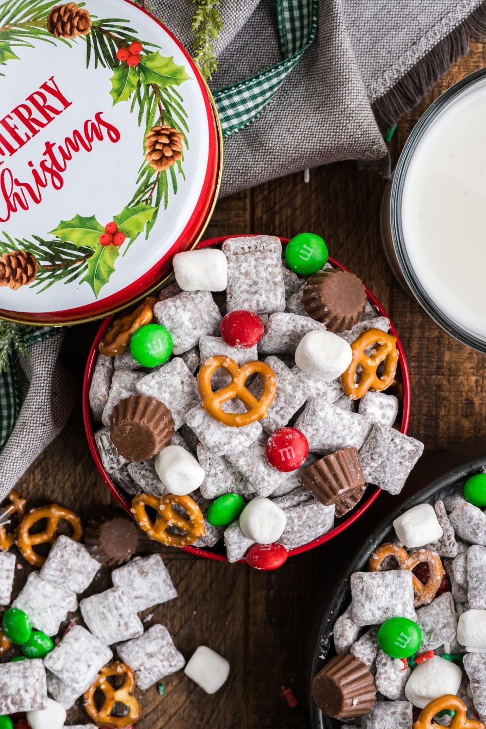 Christmas Chex Mix in bowls on table with more scattered around table and a decorative Christmas tin