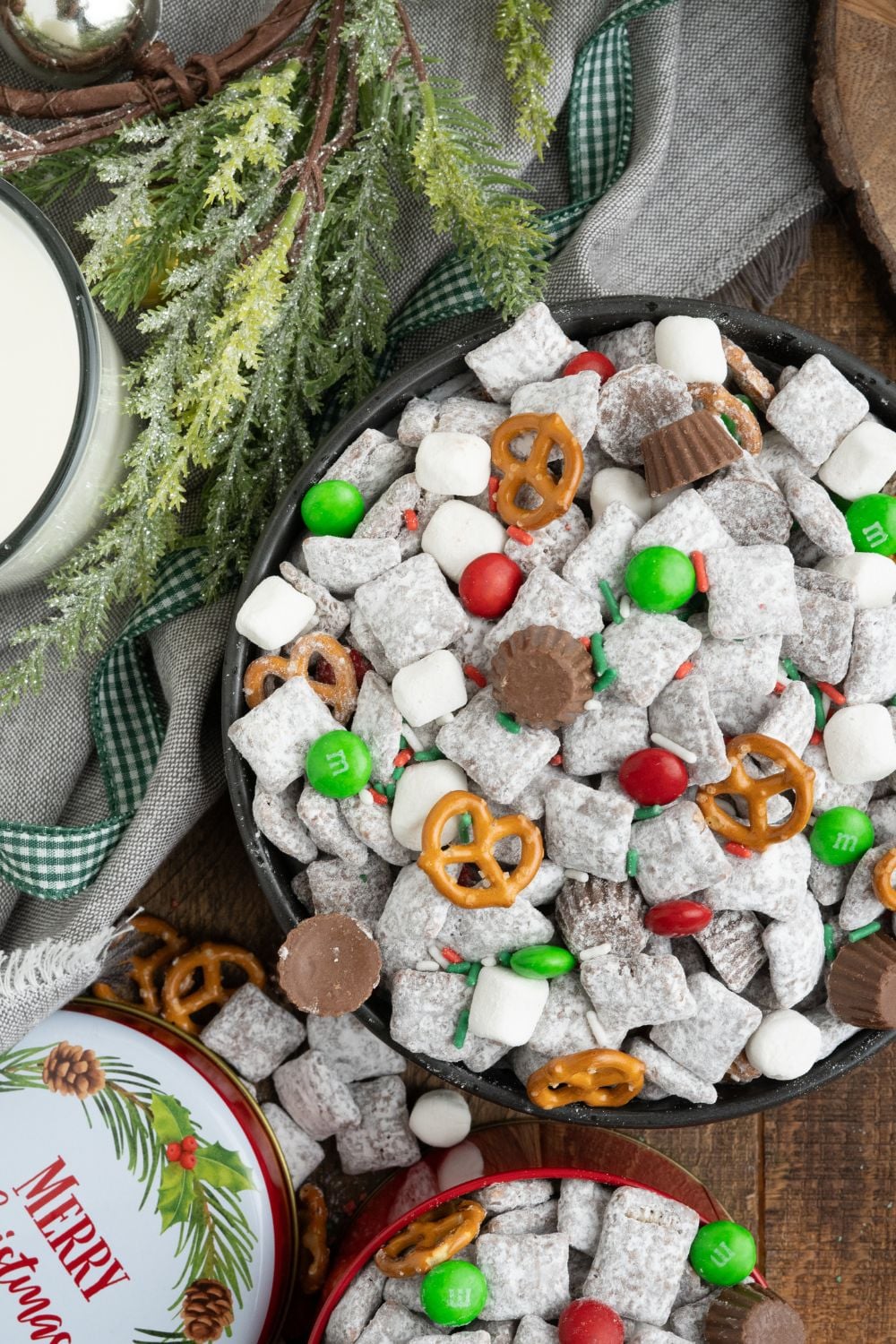 Christmas Chex Mix scattered around the table with a christmas decor to side and a glass of milk