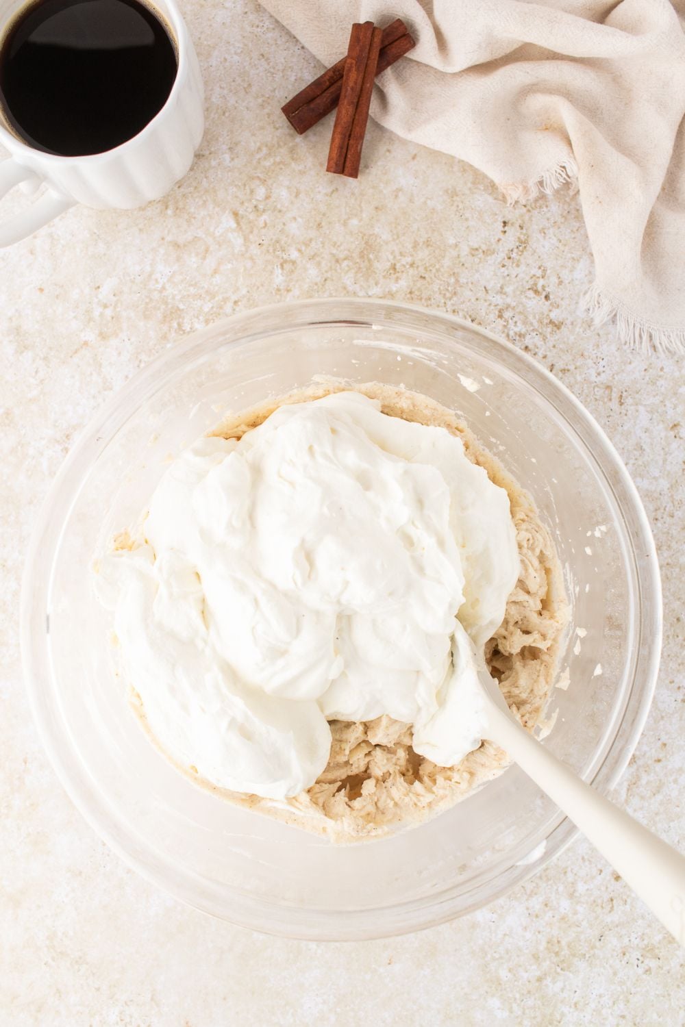 a glass bowl on table folding in whipped cream into the eggnog tiramisu