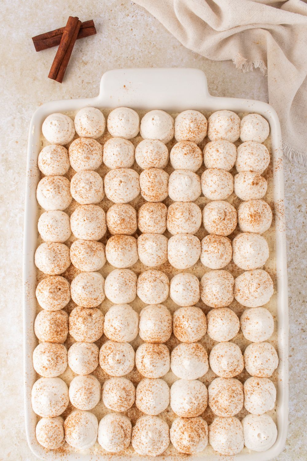 Eggnog Tiramisu in a white casserole dish on table with cinnamon sticks to the side