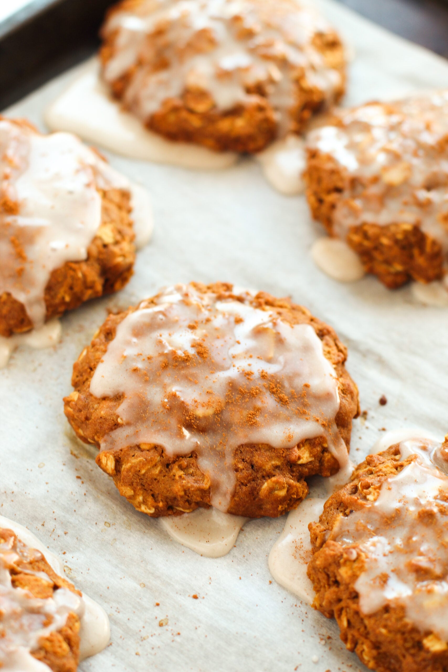 Iced Gingerbread Oatmeal Cookies on a white parchment paper lined baking cookie sheet