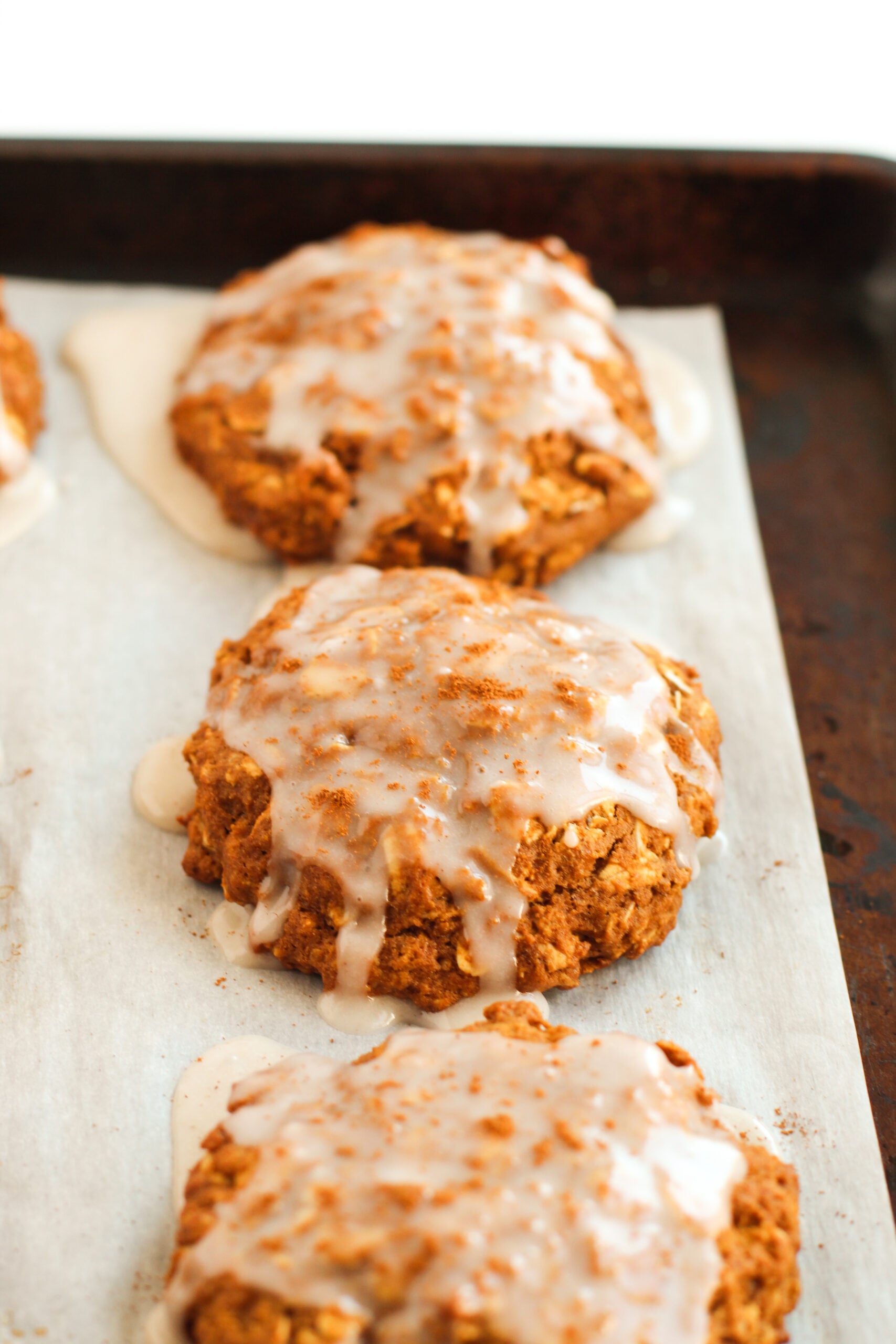 up close shot of the Iced Gingerbread Oatmeal Cookies on a lined cookie sheet tray