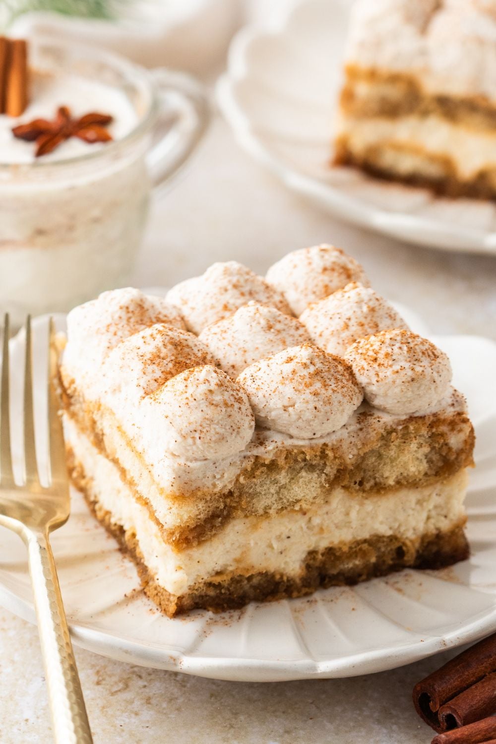 Eggnog Tiramisu sliced on white plates with a glass of eggnog behind the plate 