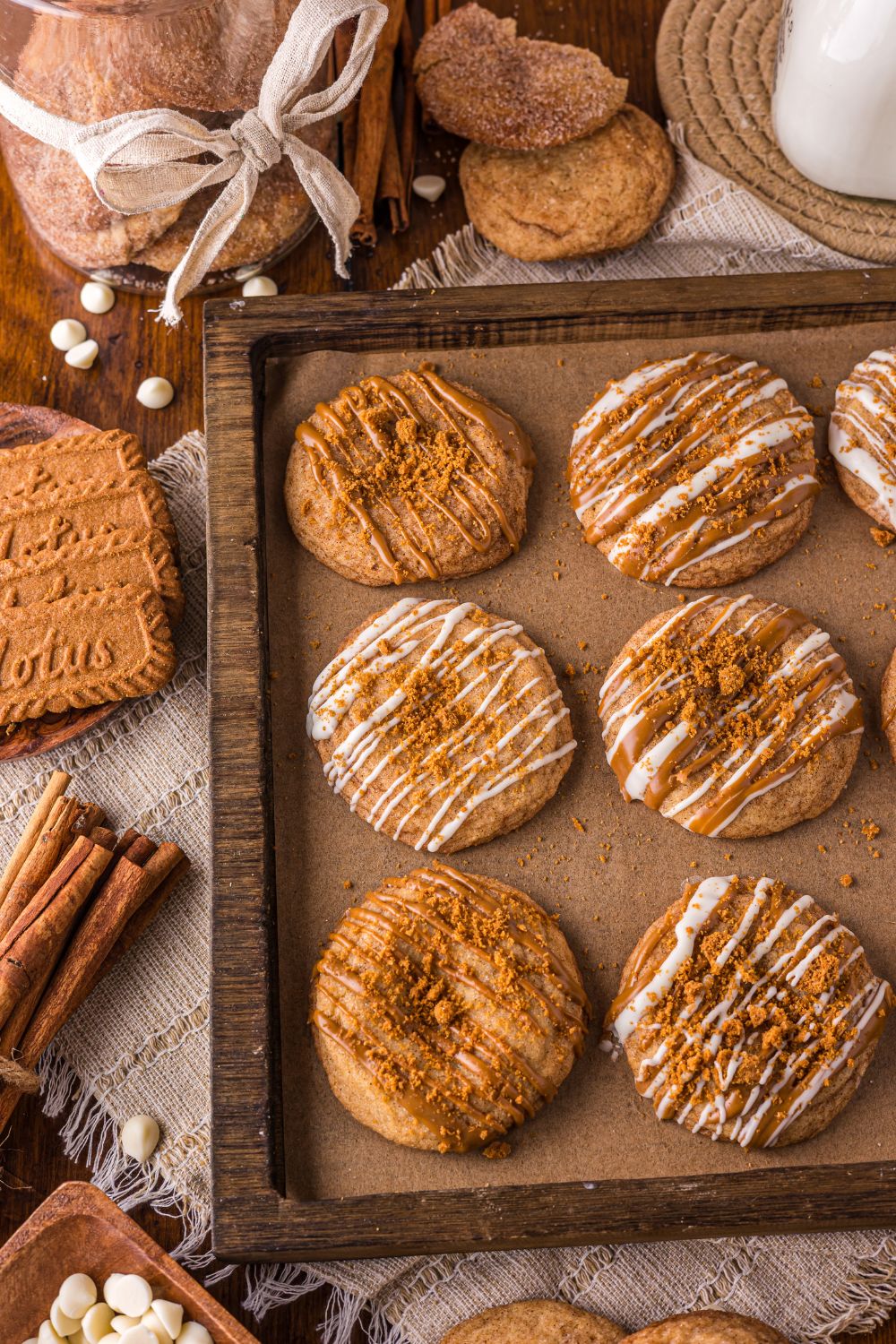 Biscoff Snickerdoodle Cookies on a baking sheet with cinnamon sticks, cookies and more around the pan on table