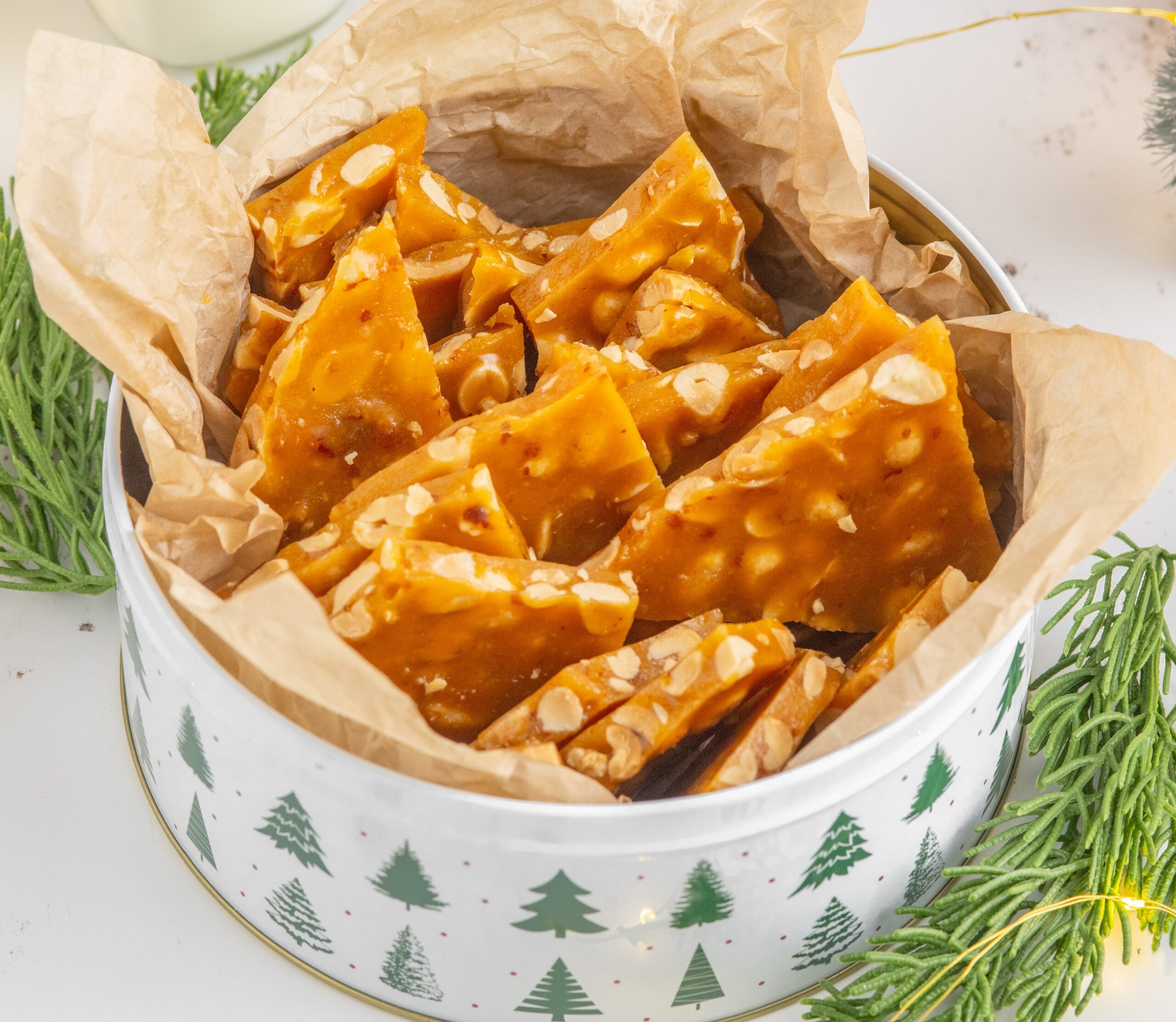 Homemade Peanut Brittle in a Christmas tin on table with Christmas decor