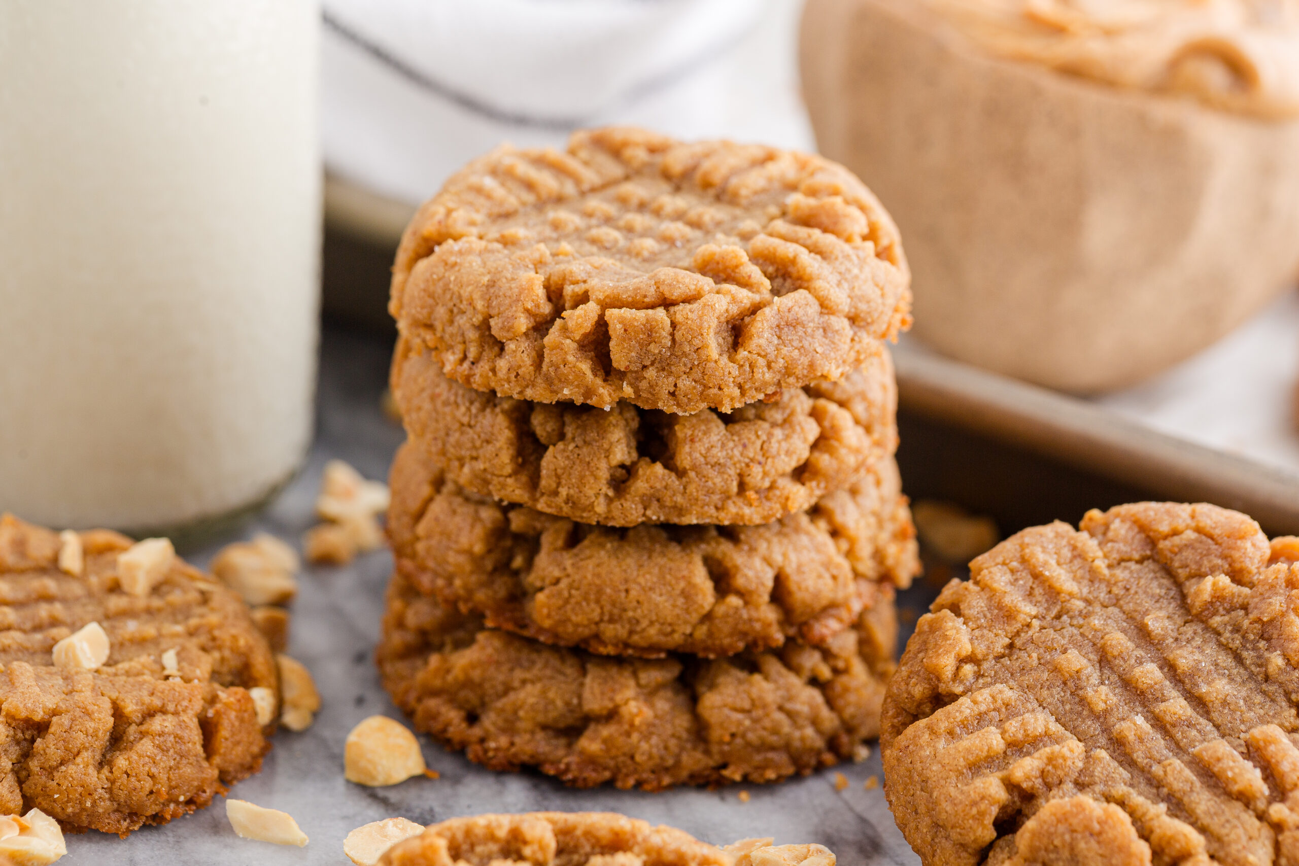 4 Ingredient Peanut Butter Cookies spread around table with a tray full of cookies behind and a tall jar of milk