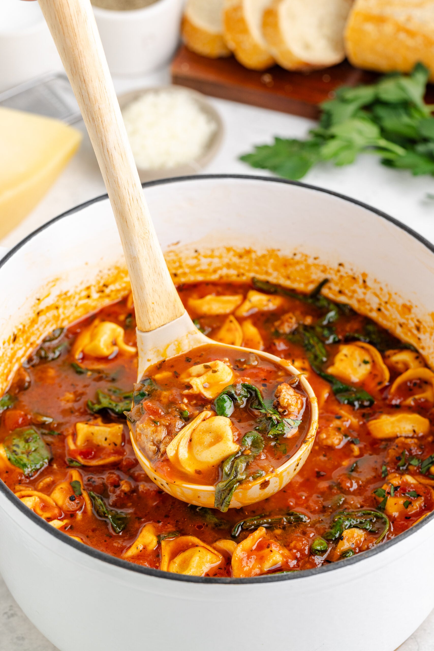 Large white pot filled with Sausage Tortellini Soup and a ladle lifting up some