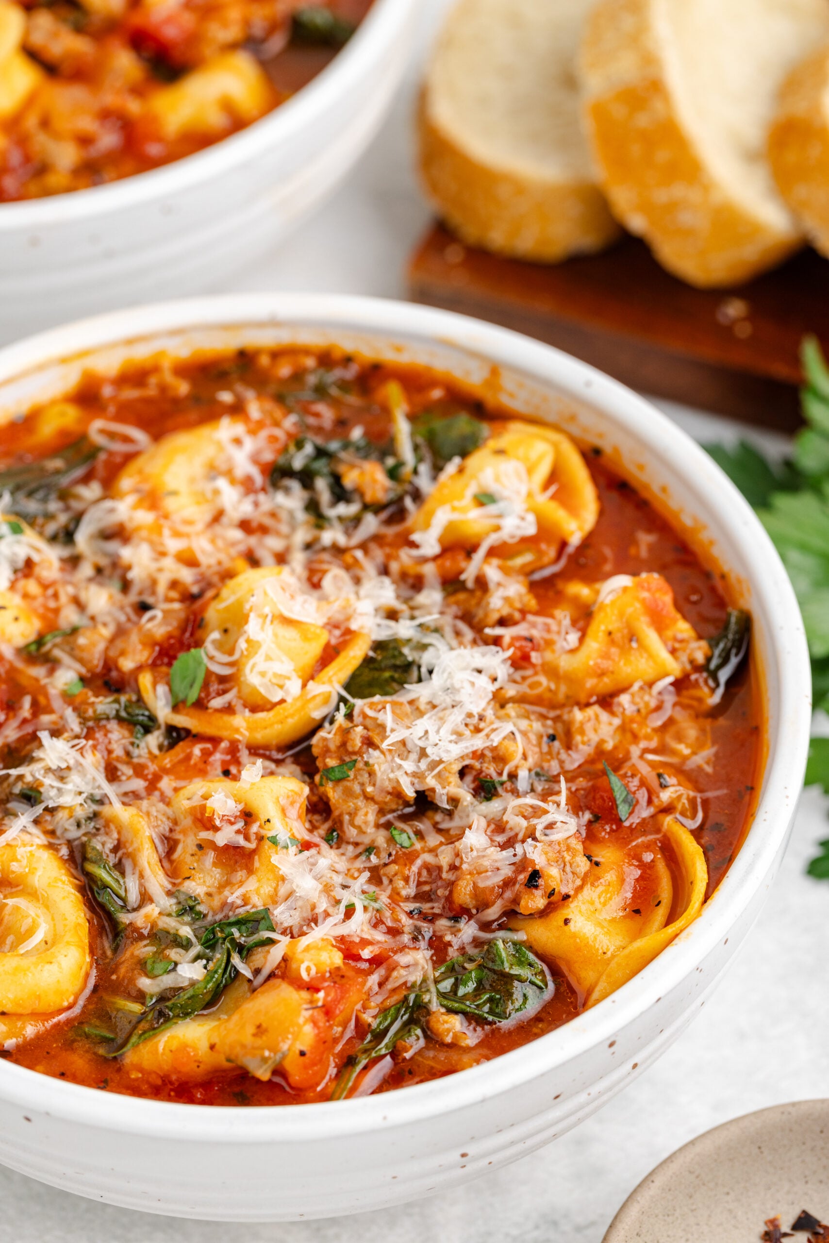 Sausage Tortellini Soup in a white bowl topped with fresh grated parmesan cheese