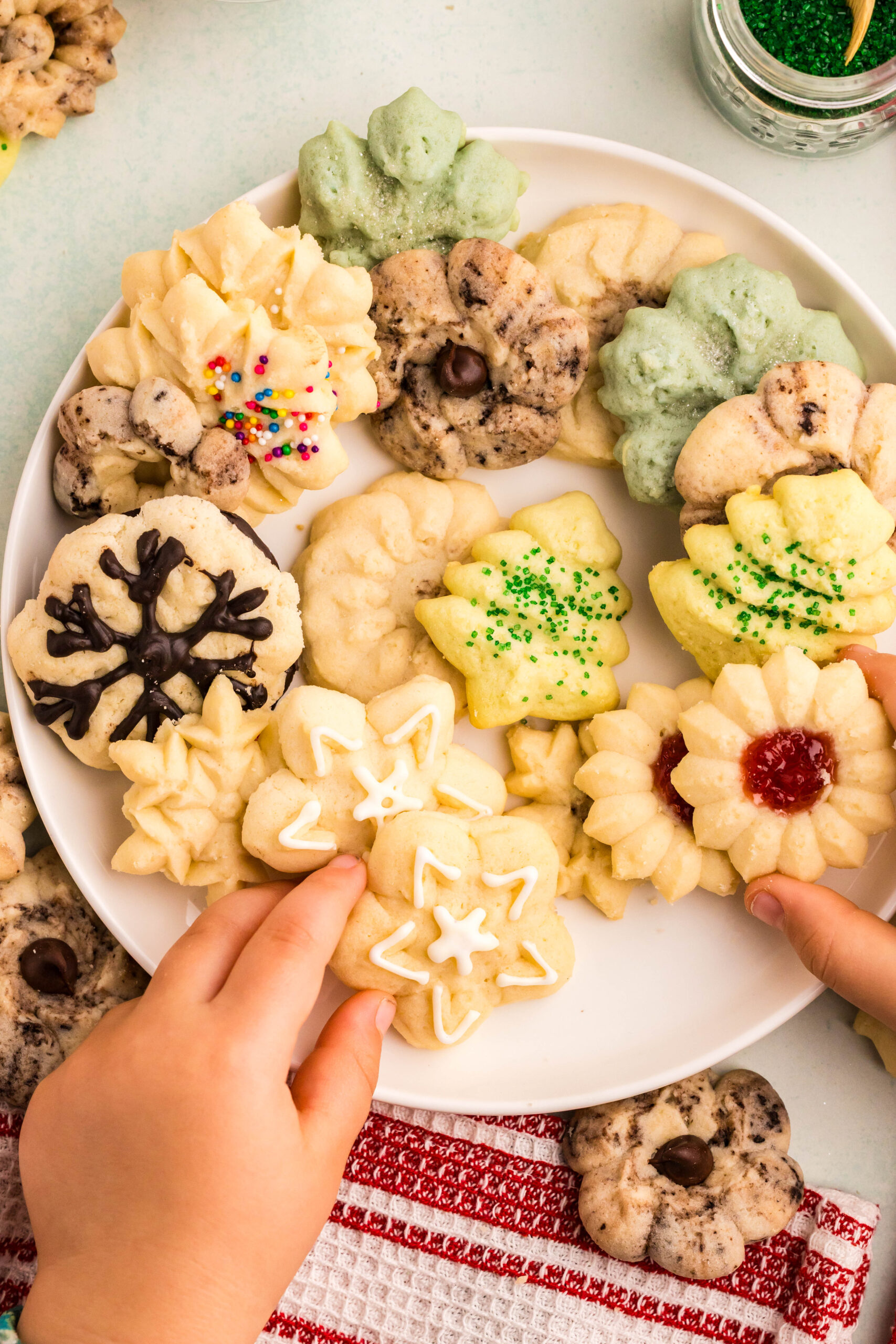 White serving plate filled with all different Spritz Christmas Cookies with a baby hand reaching for one