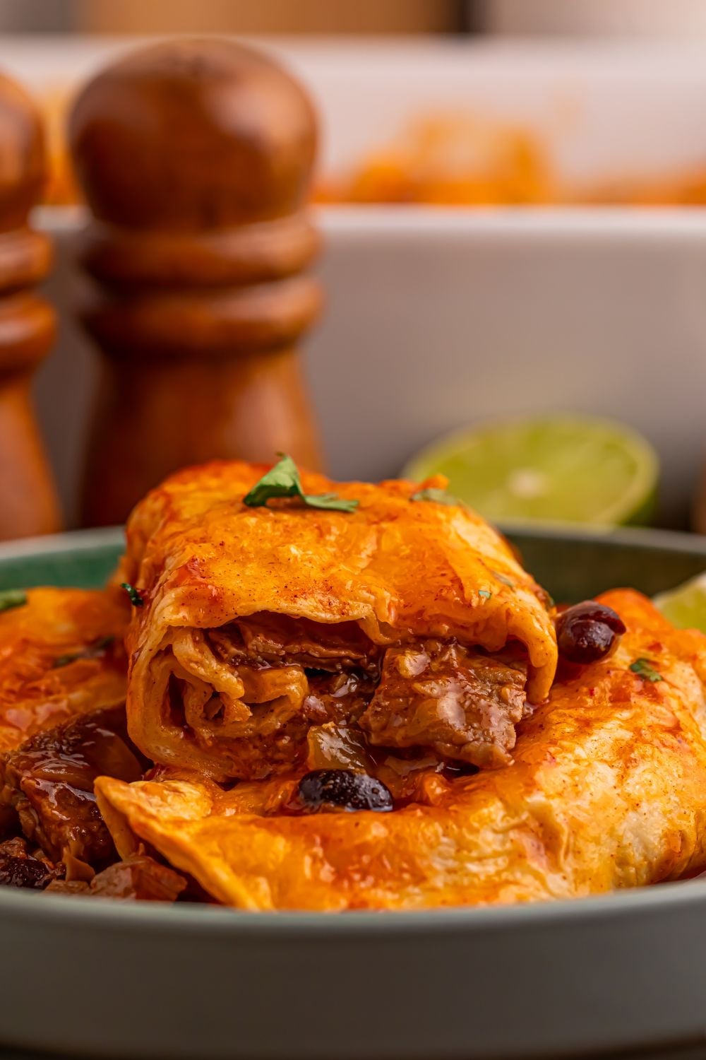 Steak Enchiladas on a grey plate on table with one cut in half sitting on top of more on a plate to show the filling of the enchiladas