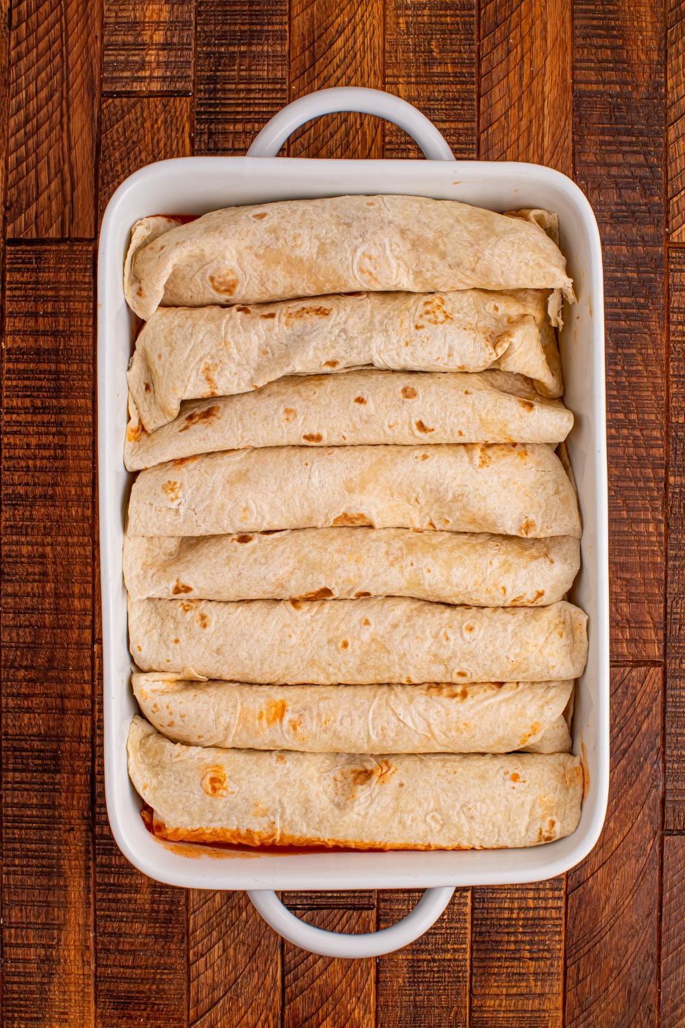 rolled enchiladas in a white casserole dish on a wooden table