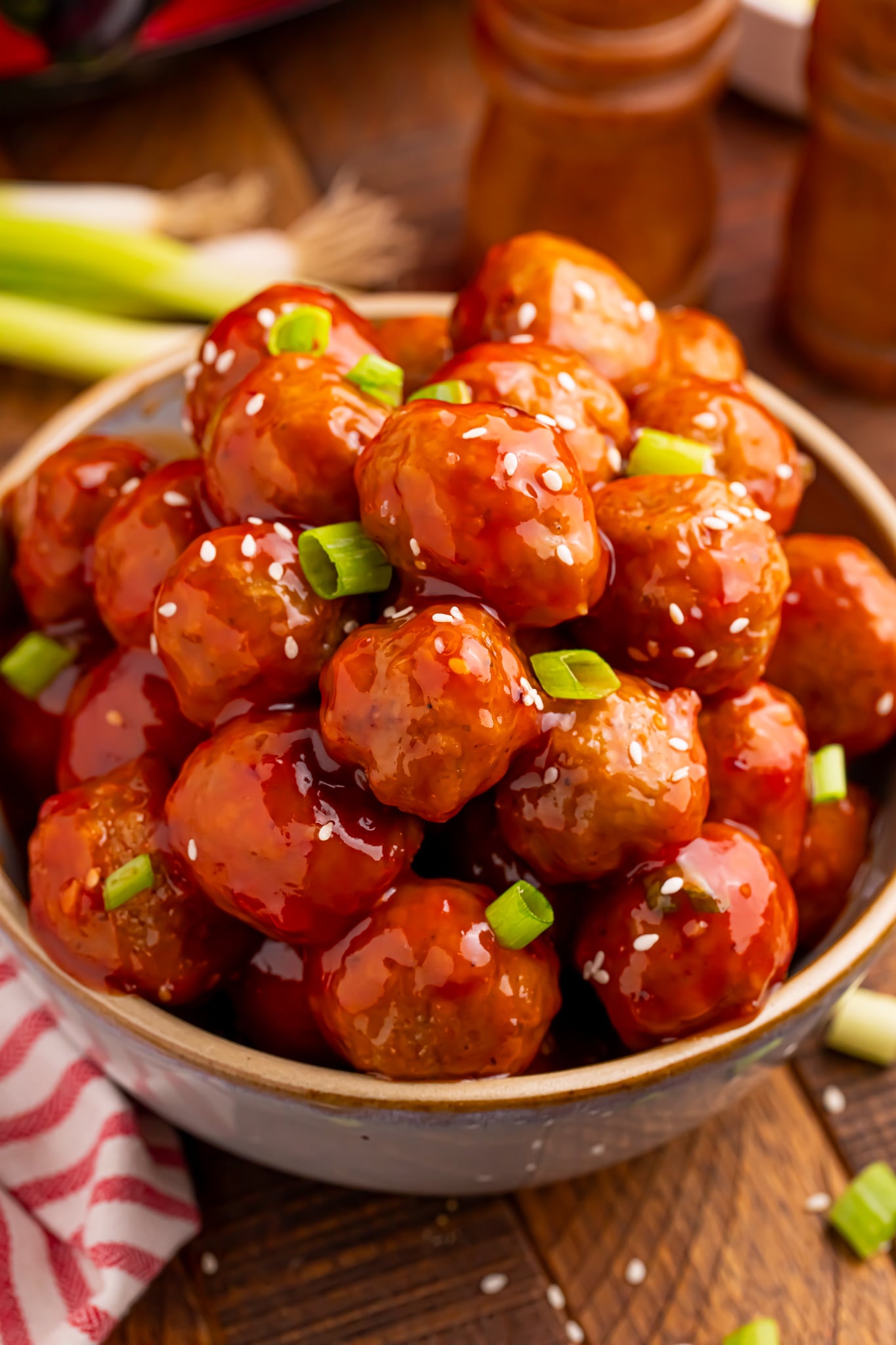 Crockpot Sweet Chili Meatballs in a wooden bowl on table with sesame seeds and green onions sprinkled on top with more onions behind it on the table