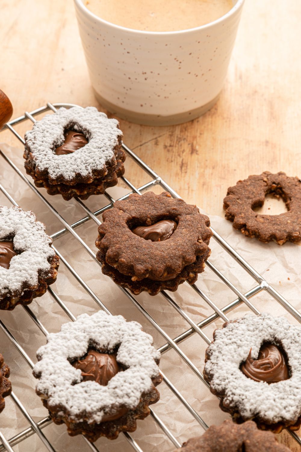 Chocolate Linzer Cookies on a cooling rack with a cup of milk to the side of the table 