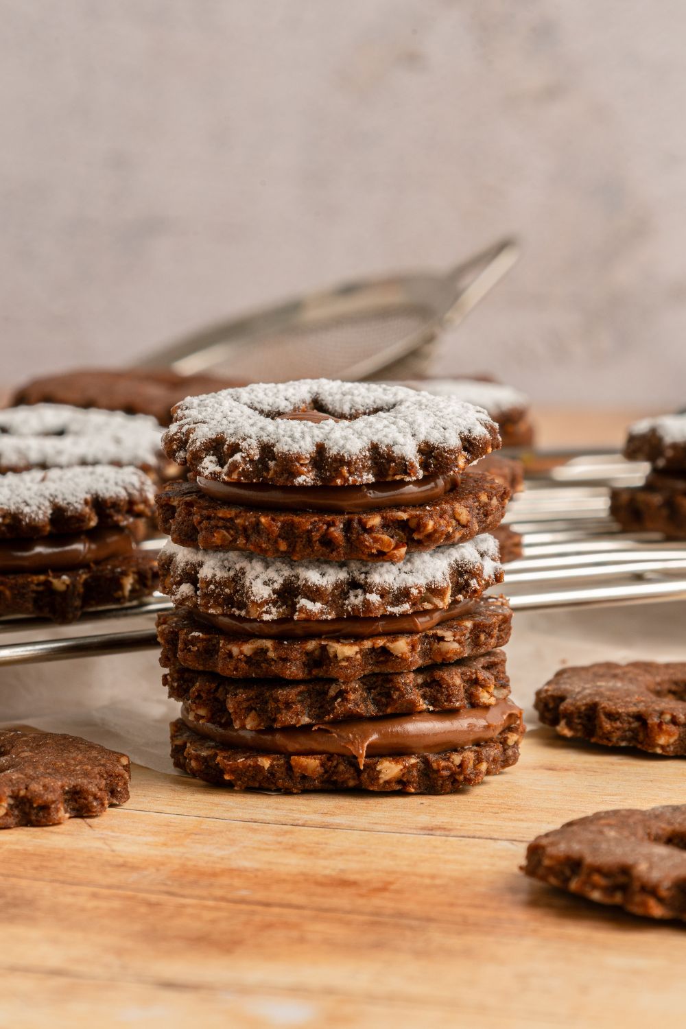 Chocolate Linzer Cookies stacked on table with more cookies around the wooden table 