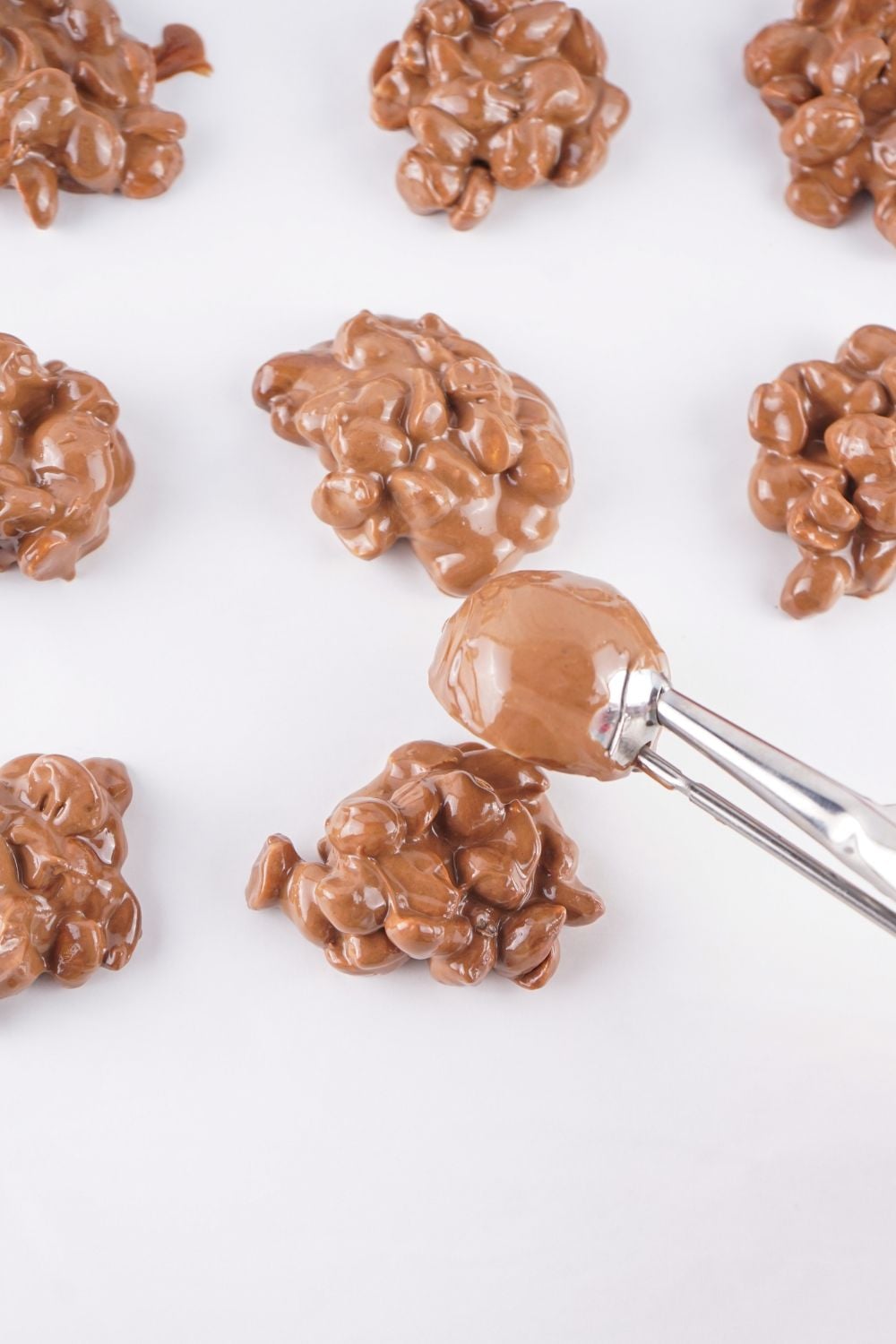 Crockpot Christmas Candy being dropped on parchment paper with cookie scoop