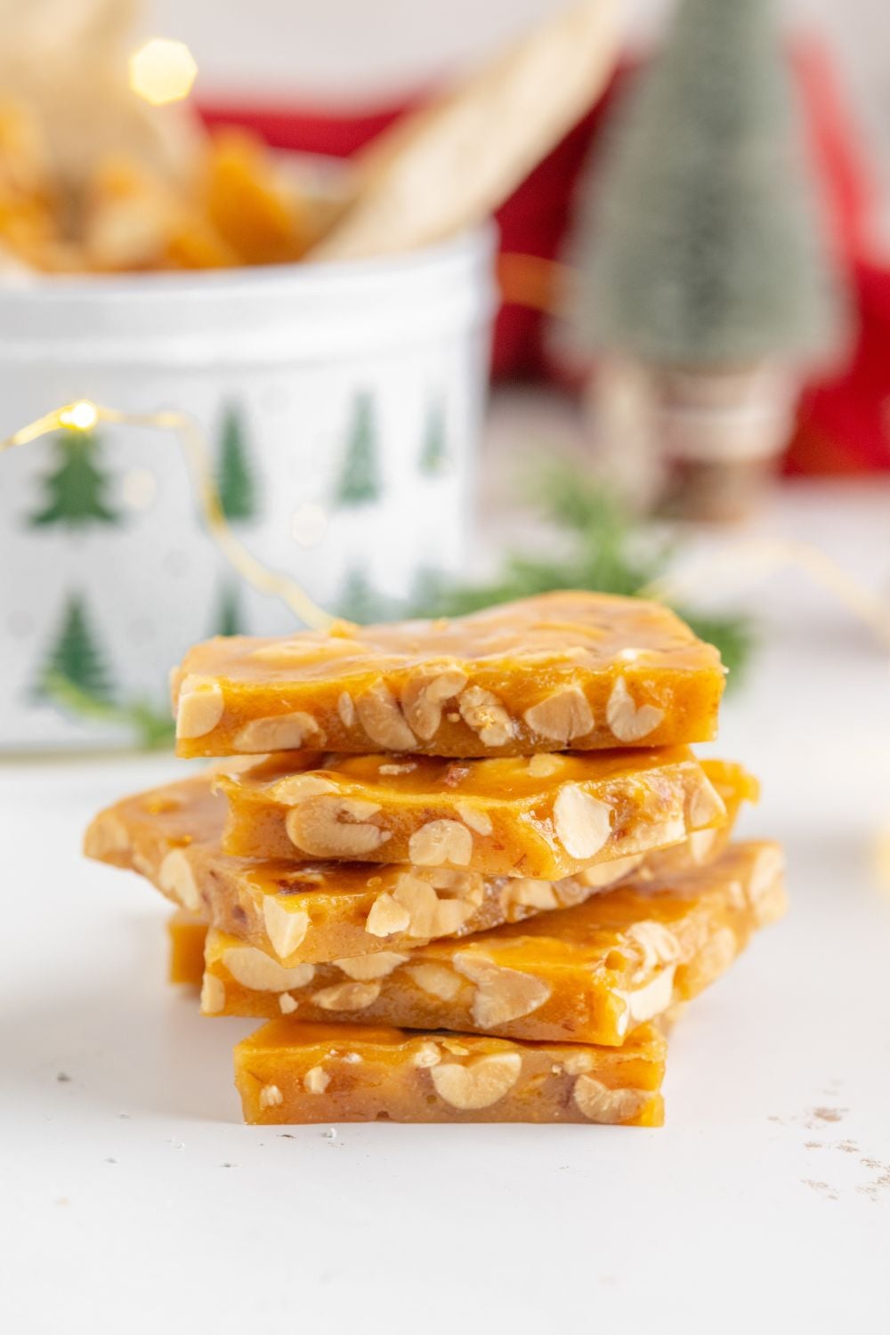a stack of Homemade Peanut Brittle on table with a tin full of more behind it on table