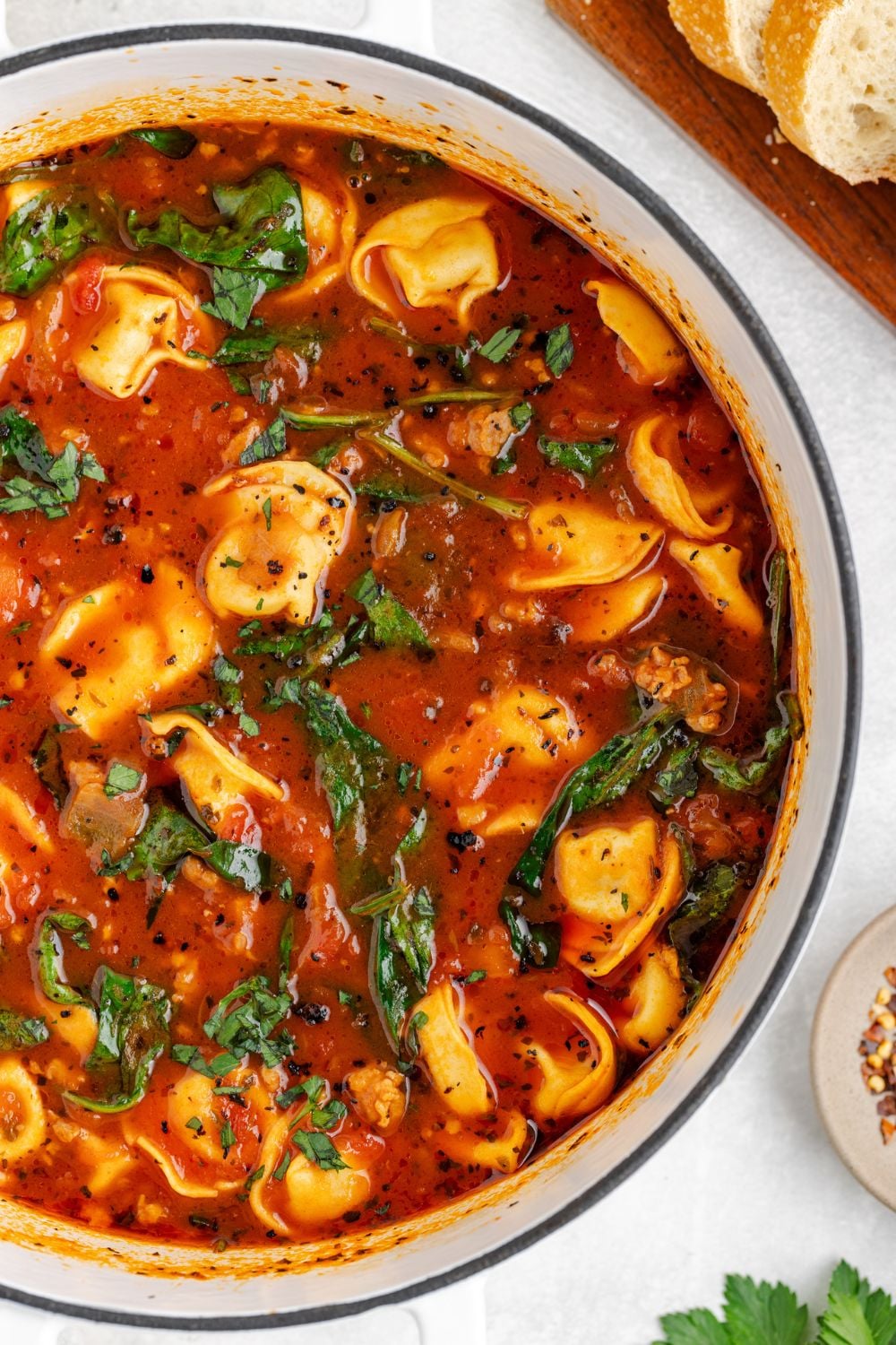 looking down at a stockpot full of Sausage Tortellini Soup sitting on a white table with some sliced French bread to side