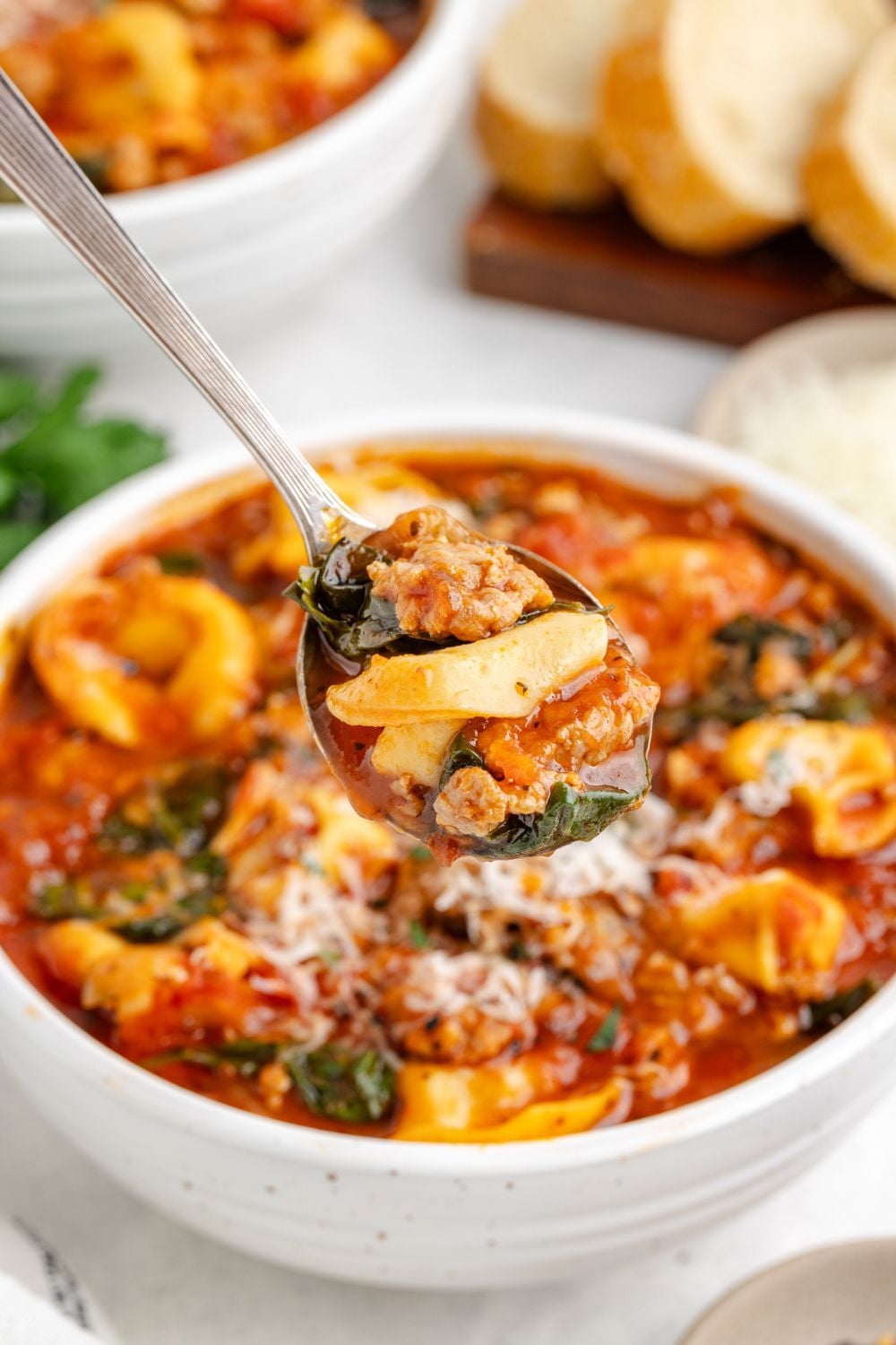 Sausage Tortellini Soup in a white bowl on table with a spoonful of soup just above the bowl